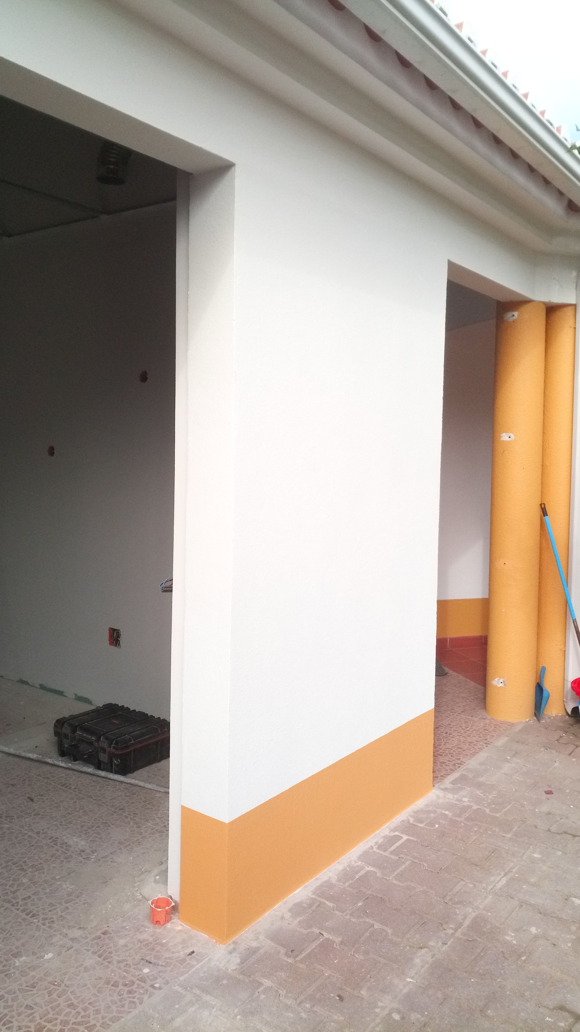 Exterior do edifício com paredes brancas, base laranja e portas abertas.