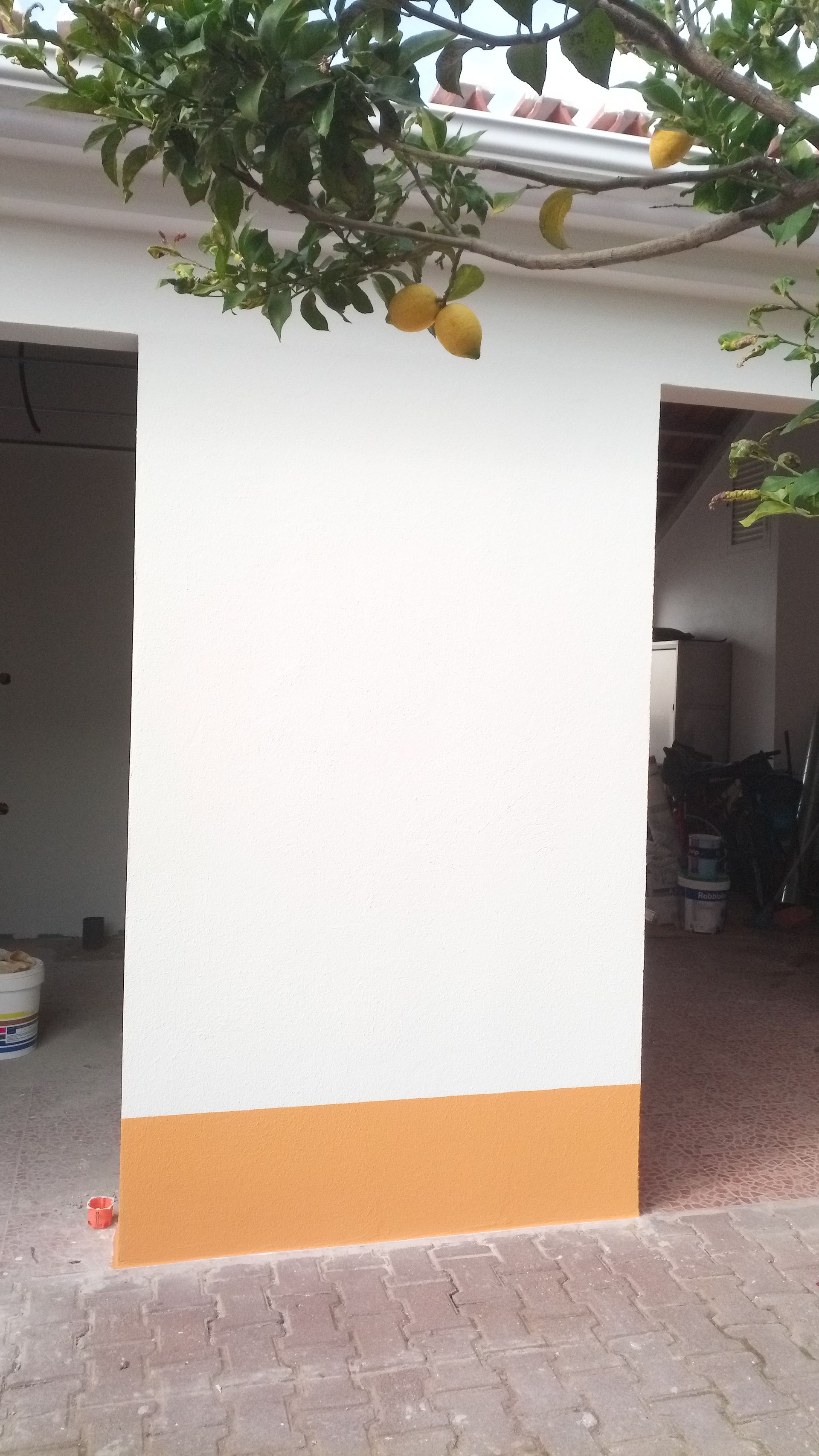 Parede de estuque branco com base laranja, sob um telhado com um limoeiro.