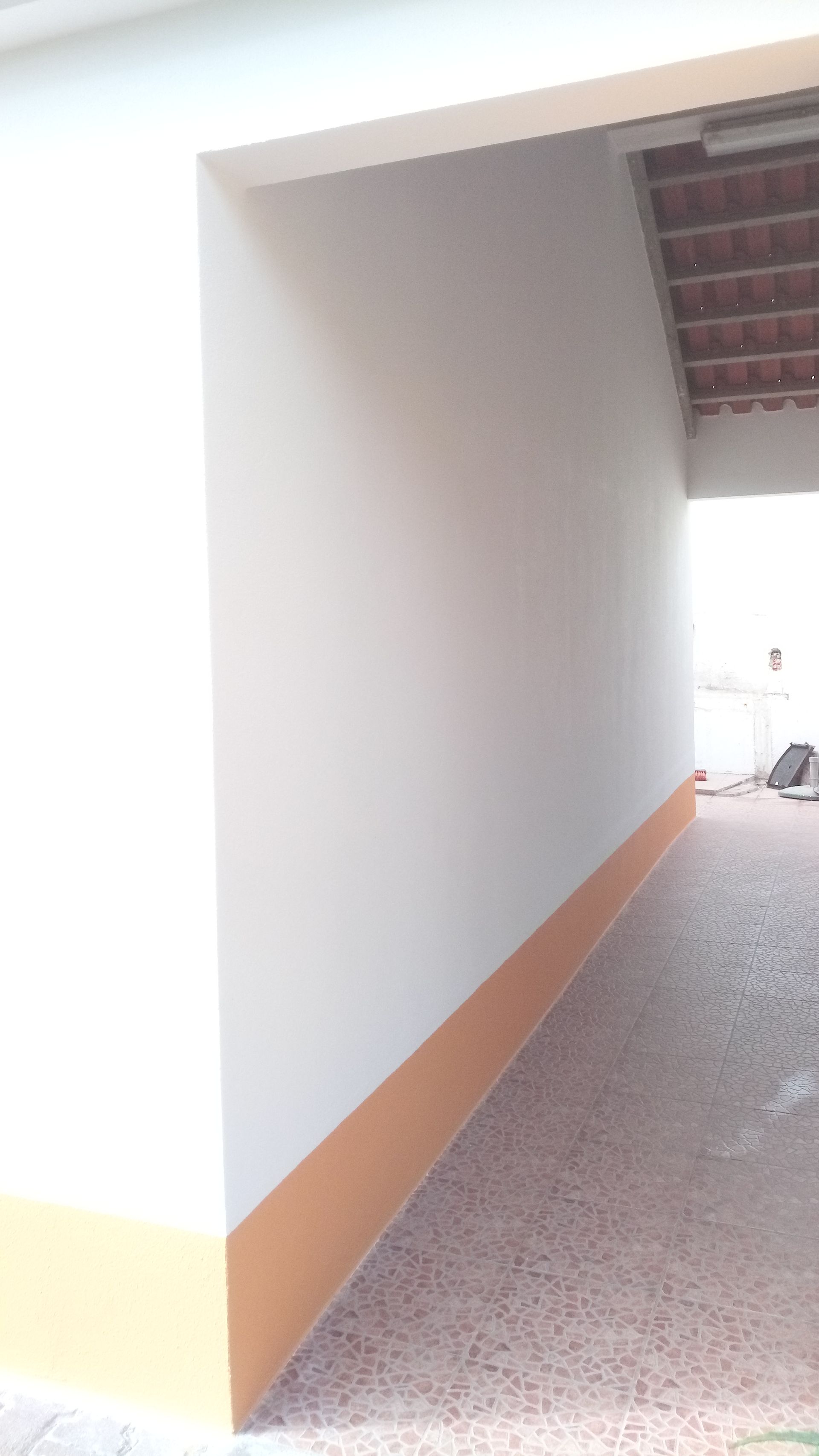 Corredor pintado de branco e bege com rodapé baixo bege e piso de azulejo.