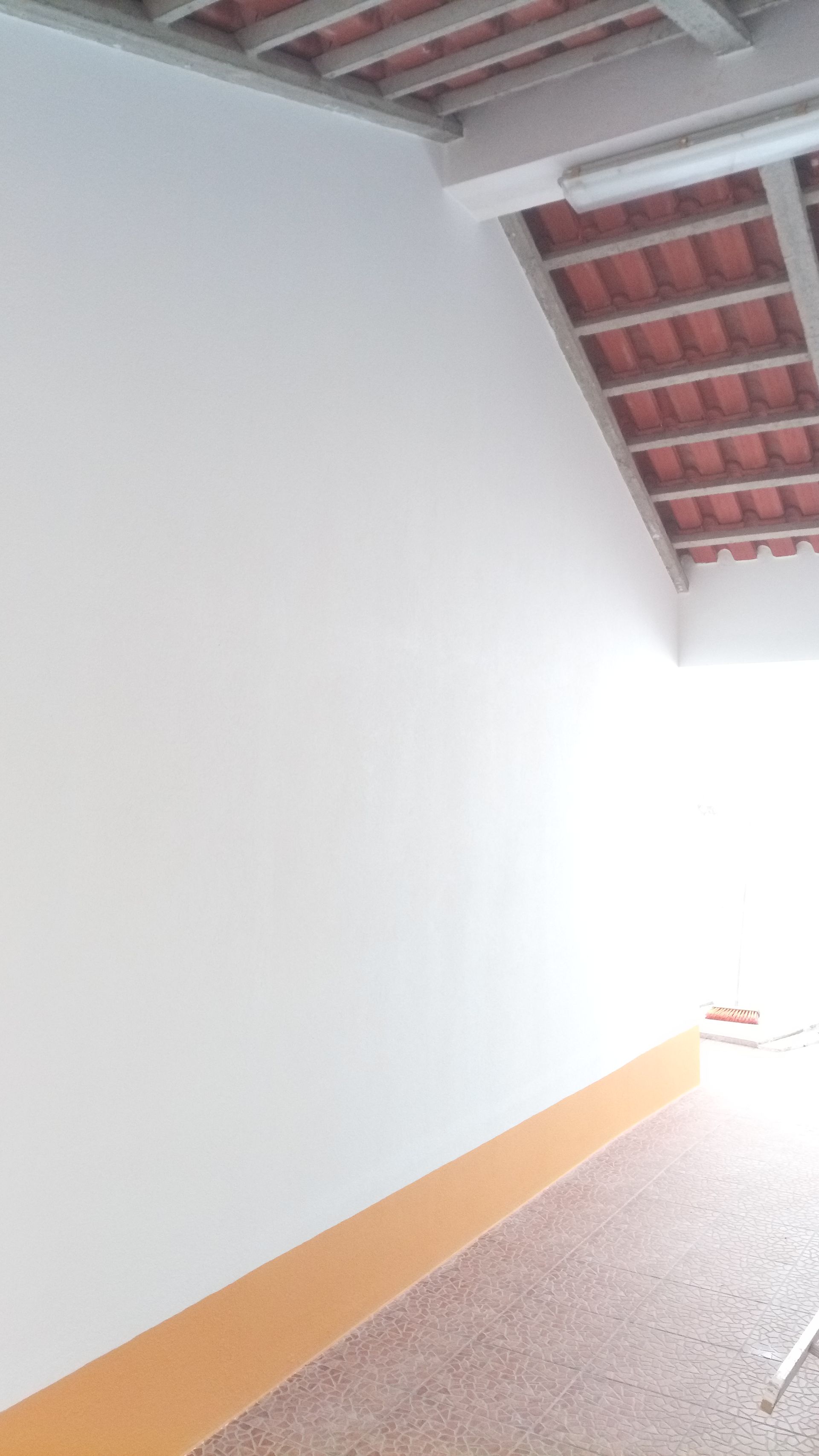 Parede branca, rodapé laranja, piso de azulejo, telhado de telha vermelha, muita luz.
