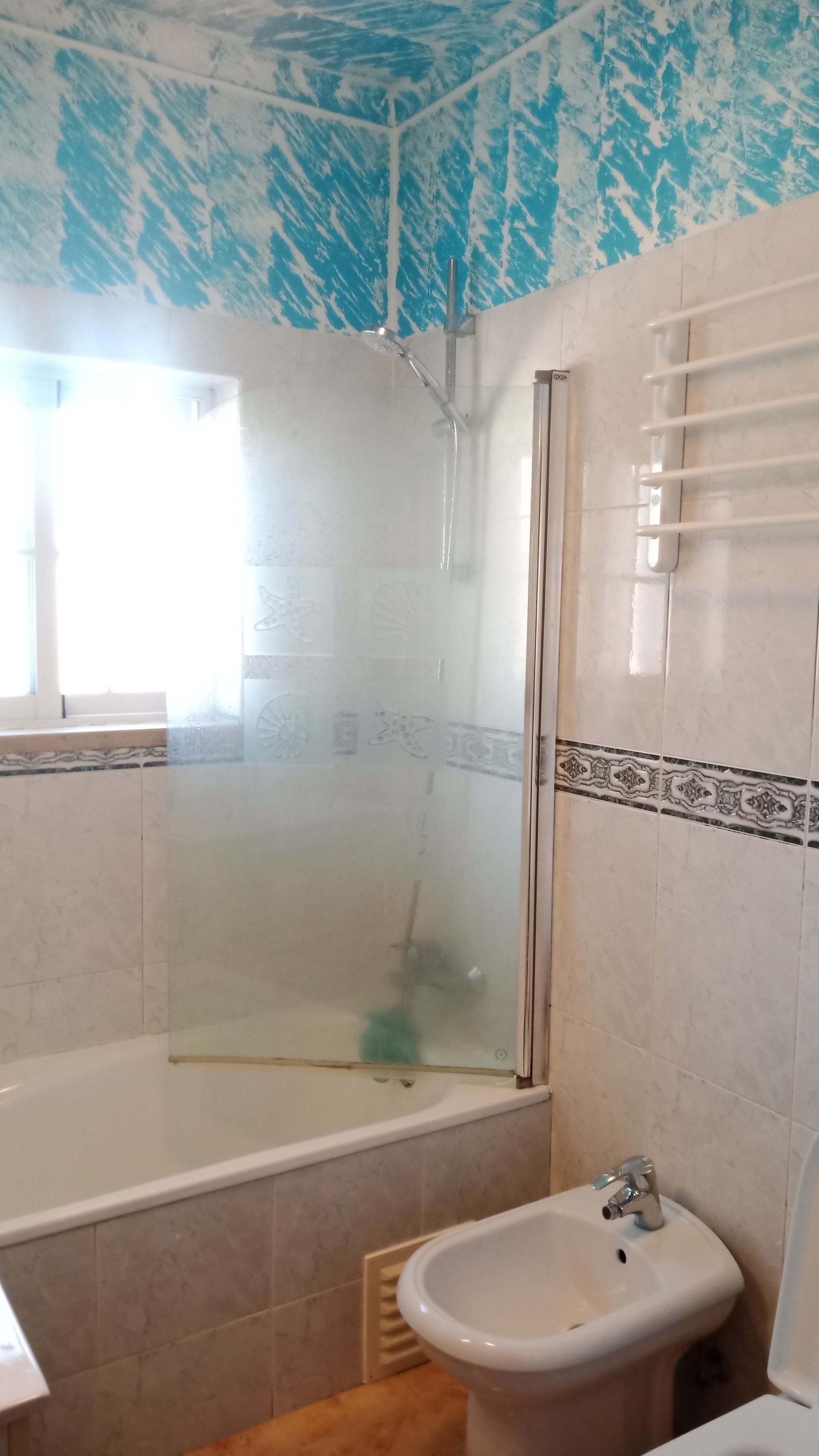 Banheiro com banheira, box para chuveiro, bidê e paredes revestidas com azulejos azuis e brancos.