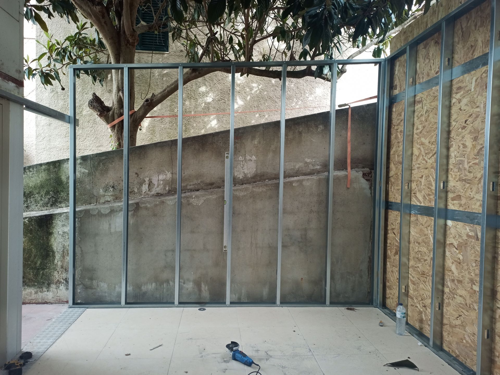 Estrutura metálica na parede contra uma parede de concreto, com alguns painéis de madeira à direita.