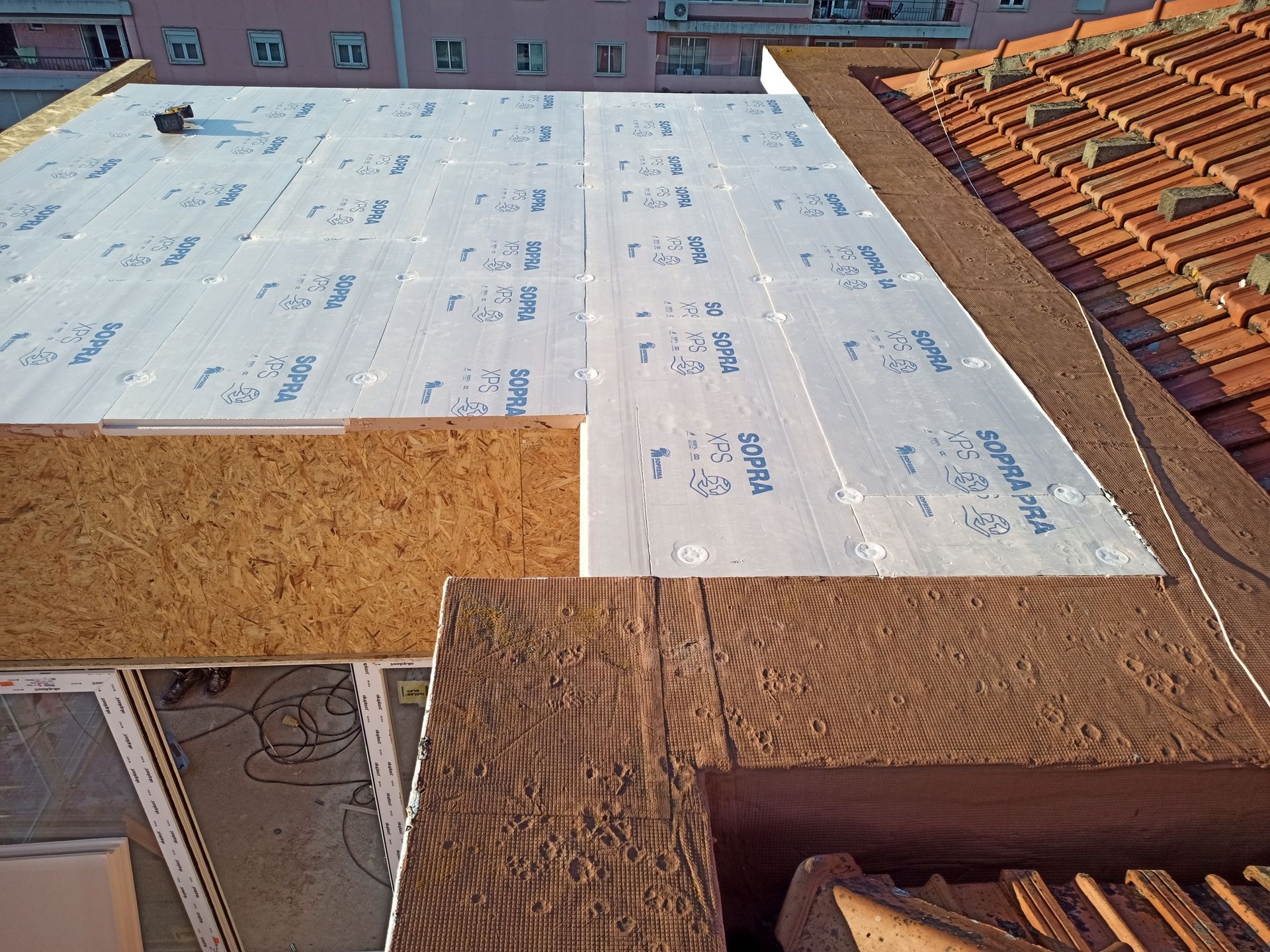 Construção do telhado: camadas de isolamento, madeira compensada e vigas de madeira sobre o telhado de telha existente.