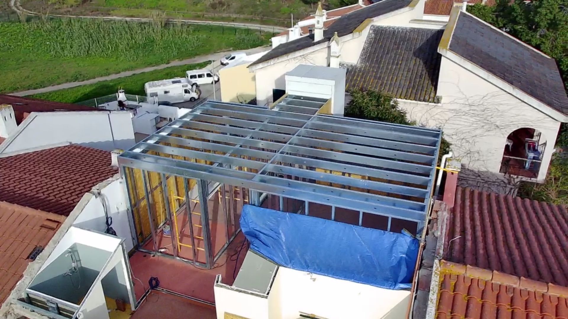 Vista aérea de uma estrutura metálica construída em um telhado, com uma lona azul cobrindo uma parte dela.
