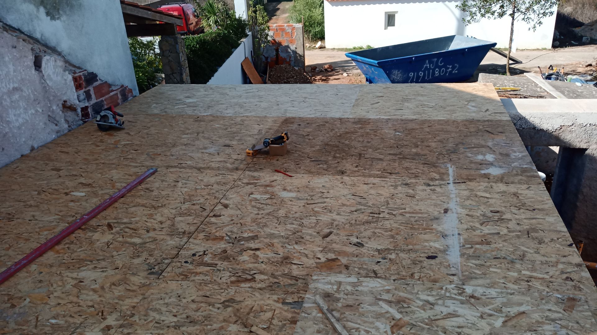 Placas de OSB colocadas em um telhado, ferramentas e entulho por perto. Uma banheira azul está ao fundo.