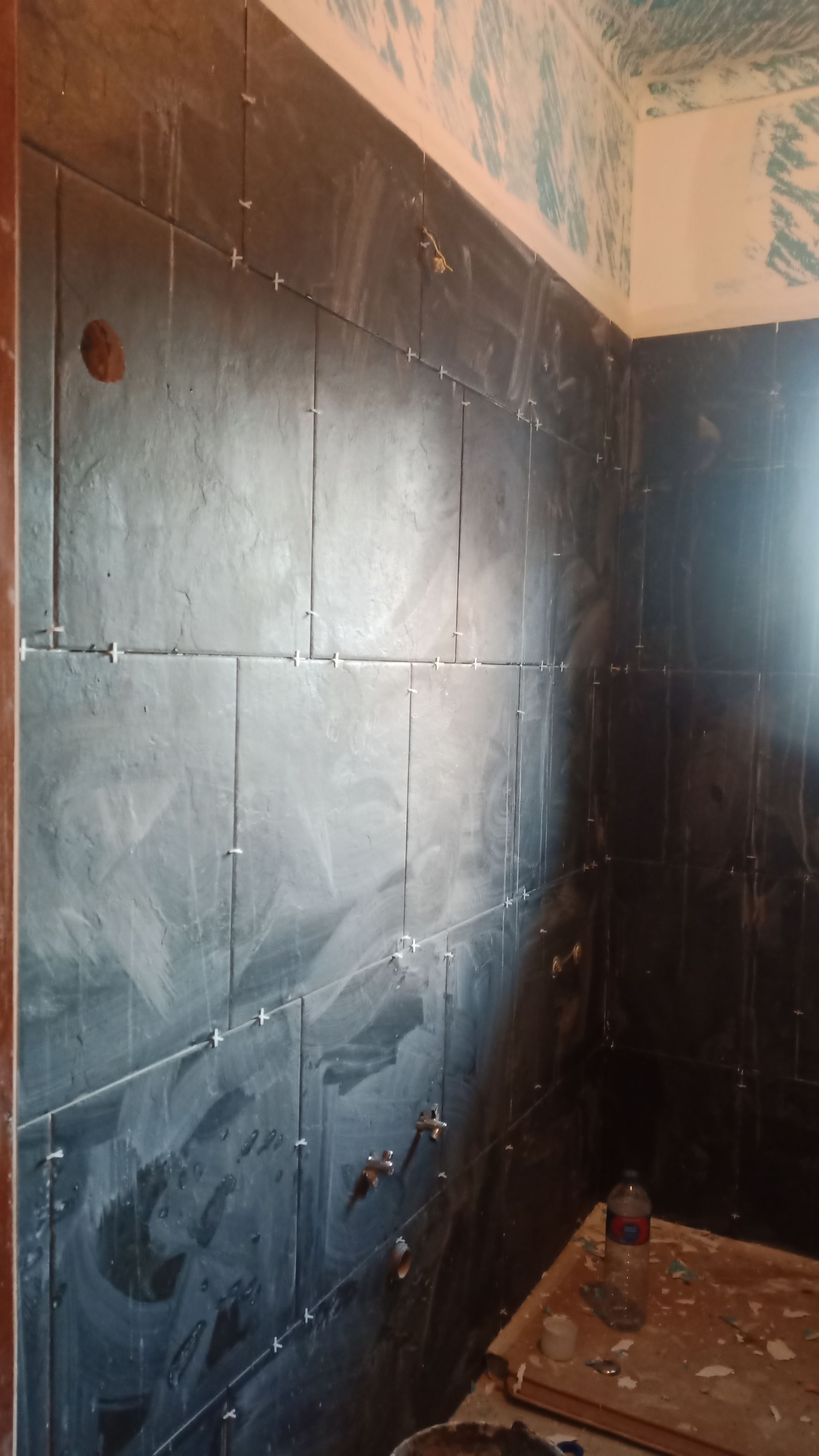 Azulejos cinza-escuros instalados na parede de um banheiro, com espaçadores.