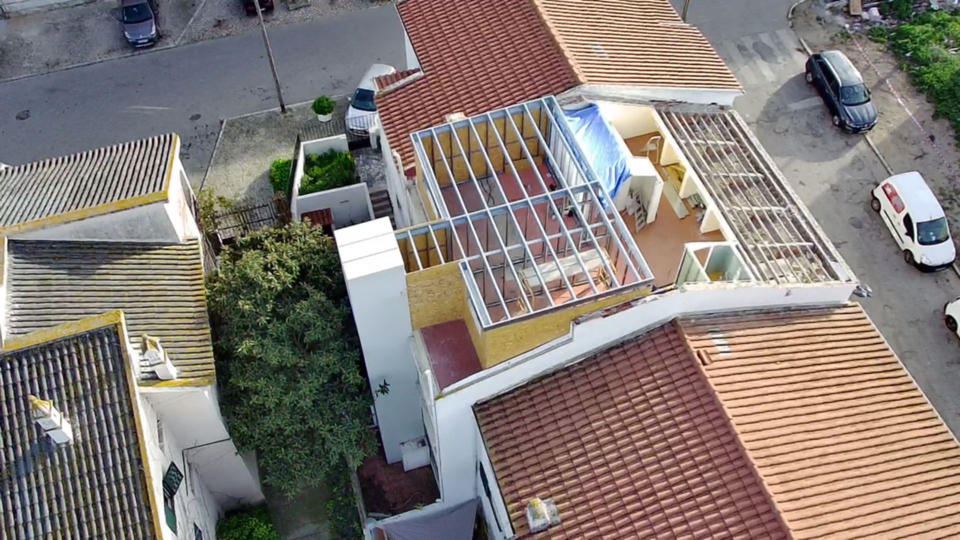 Vista aérea de edifícios com telhados de telha vermelha, fachada branca e um terraço na cobertura com uma lona azul.