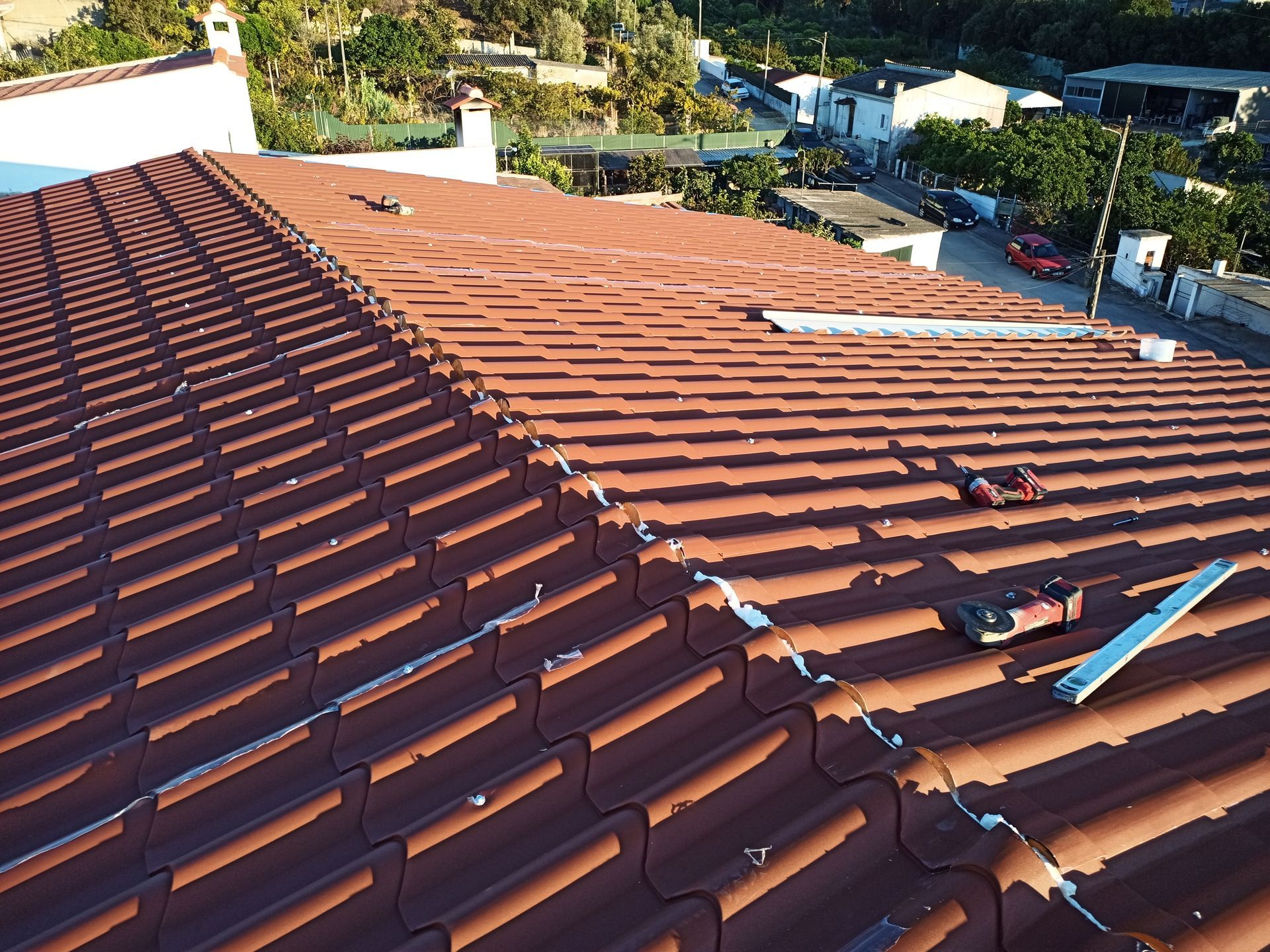 Telhado de telha vermelha com ferramentas, com vista para um bairro.