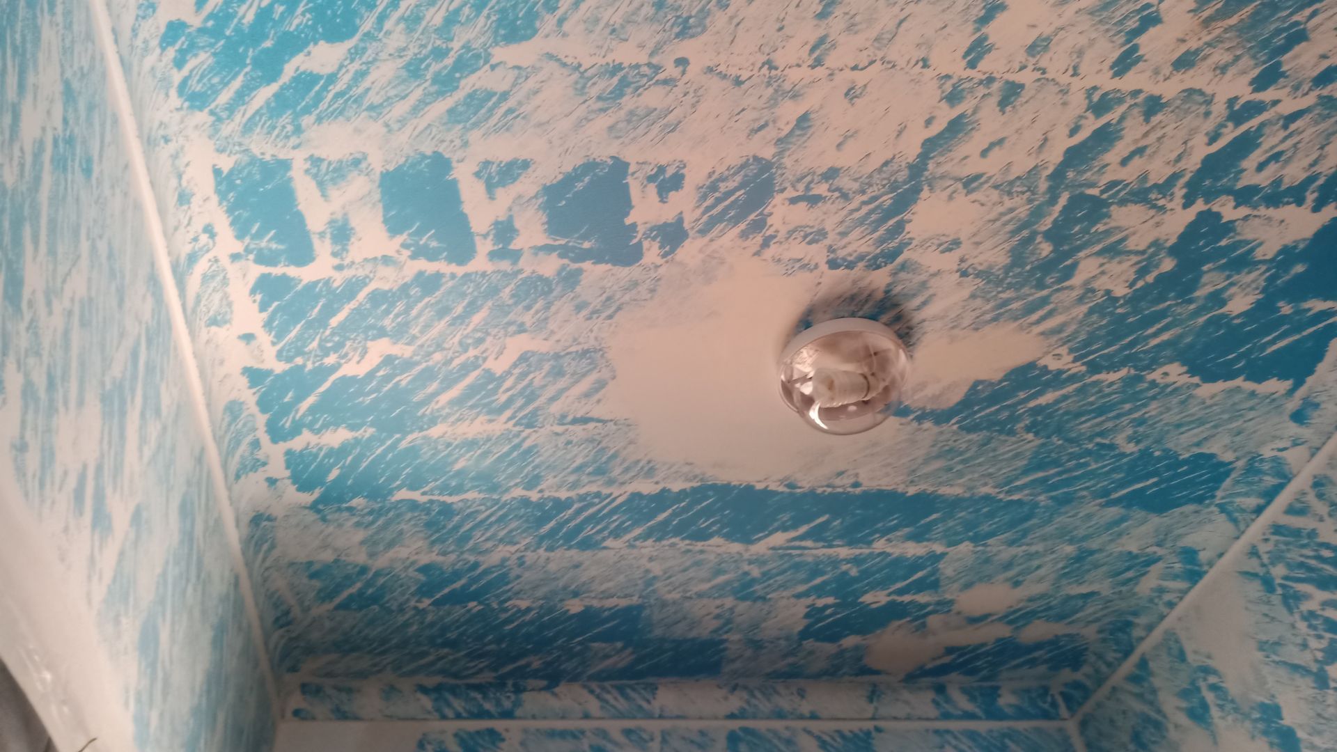 Teto azul com um desenho texturizado branco e uma luminária redonda.