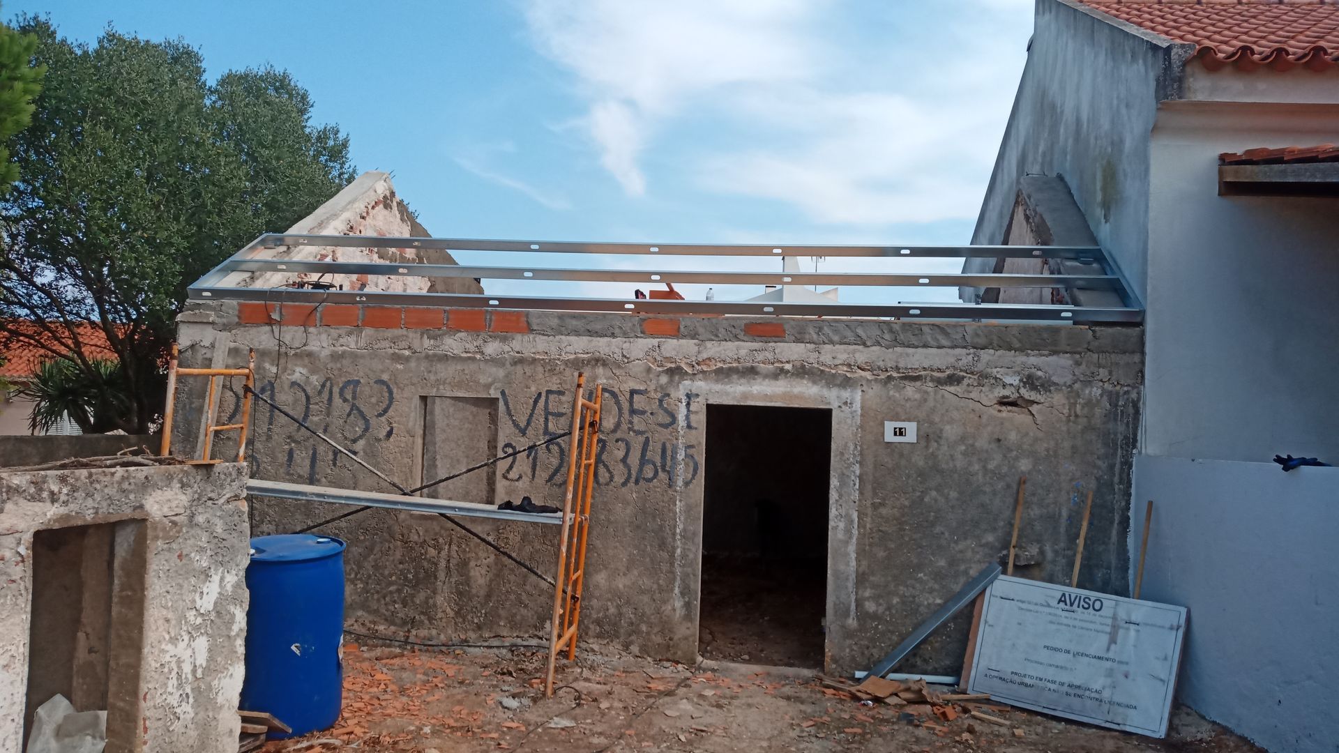 Prédio em construção com vigas metálicas expostas no telhado, pichações e entulho.