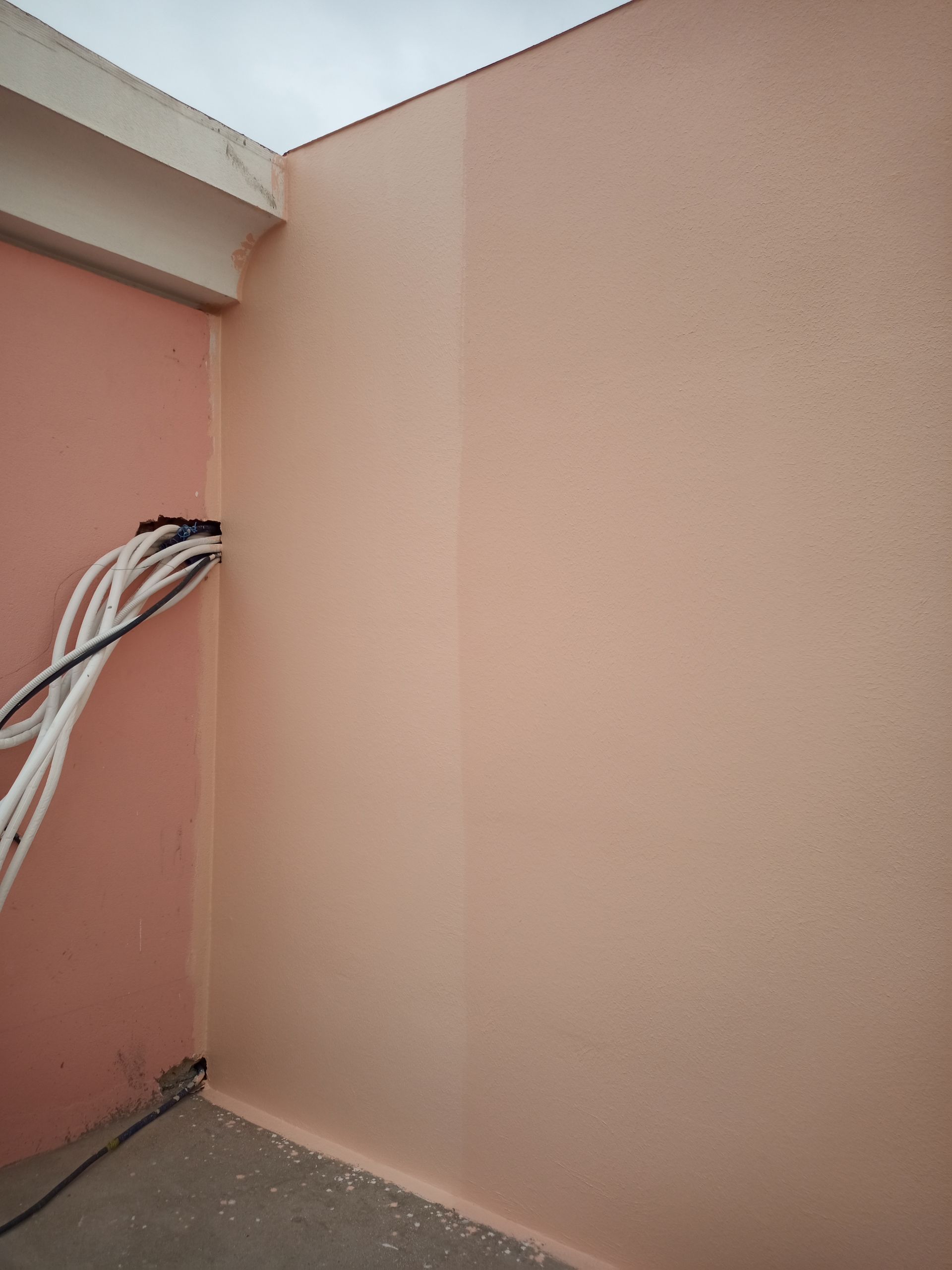 Canto de uma sala cor de pêssego com cabos elétricos brancos e uma viga branca no teto.