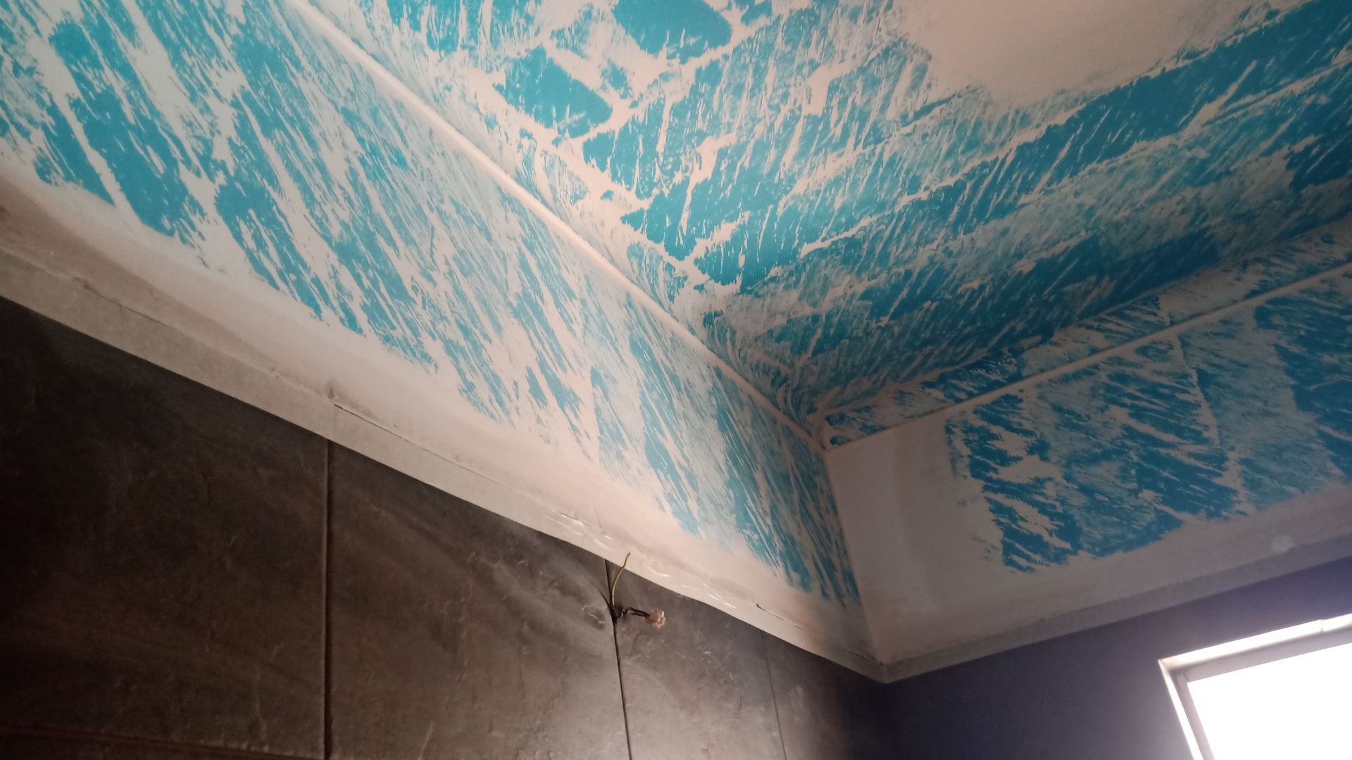 Teto pintado de azul com detalhes em branco e uma seção de parede revestida com azulejos escuros.