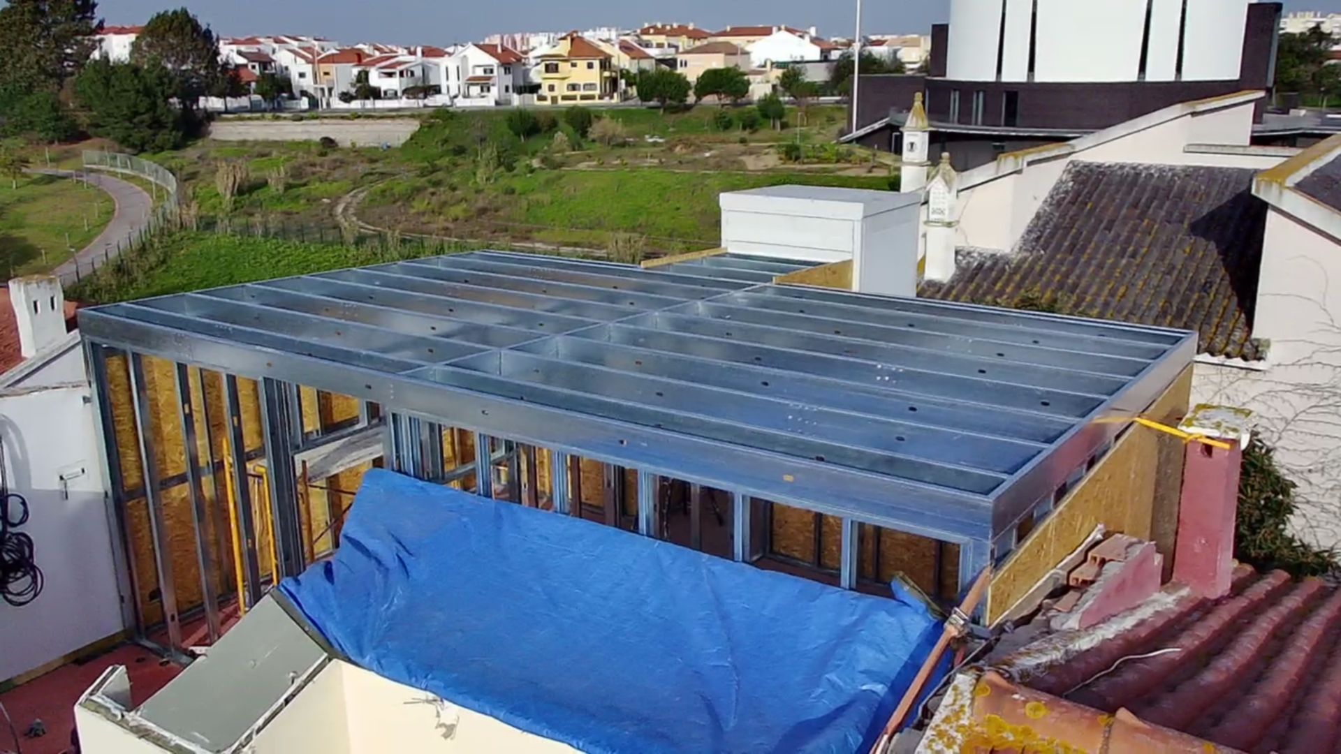 Estrutura metálica para a cobertura de um prédio em construção, em um edifício antigo, lona azul, casas ao fundo.