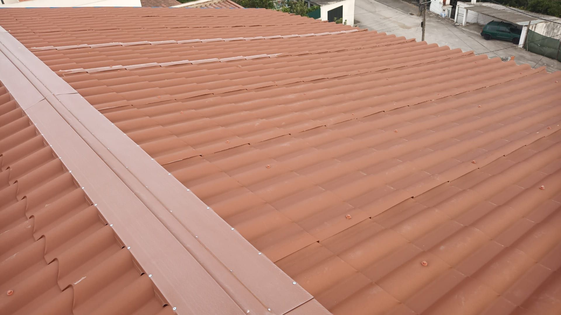 Telhado de telha ondulada vermelha com uma longa faixa metálica marrom.