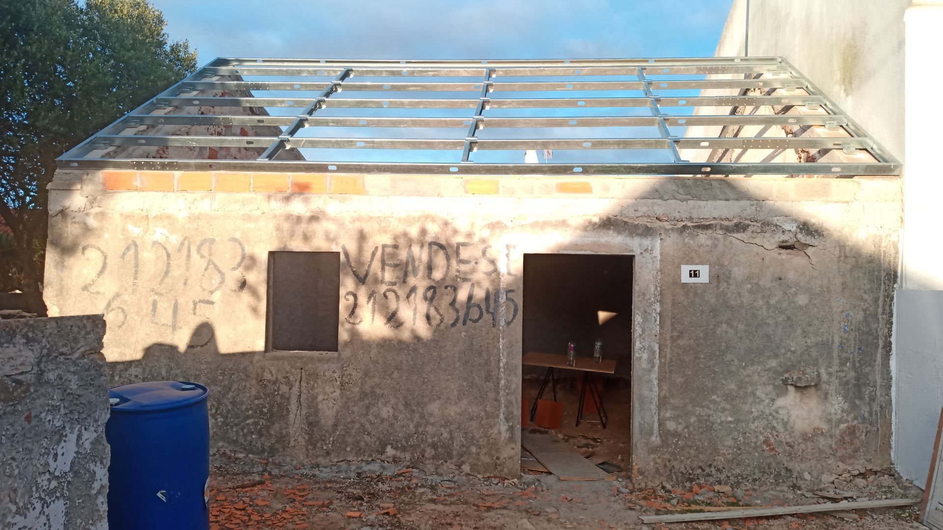 Galpão de concreto em construção com estrutura metálica do telhado exposta; grafite na parede.