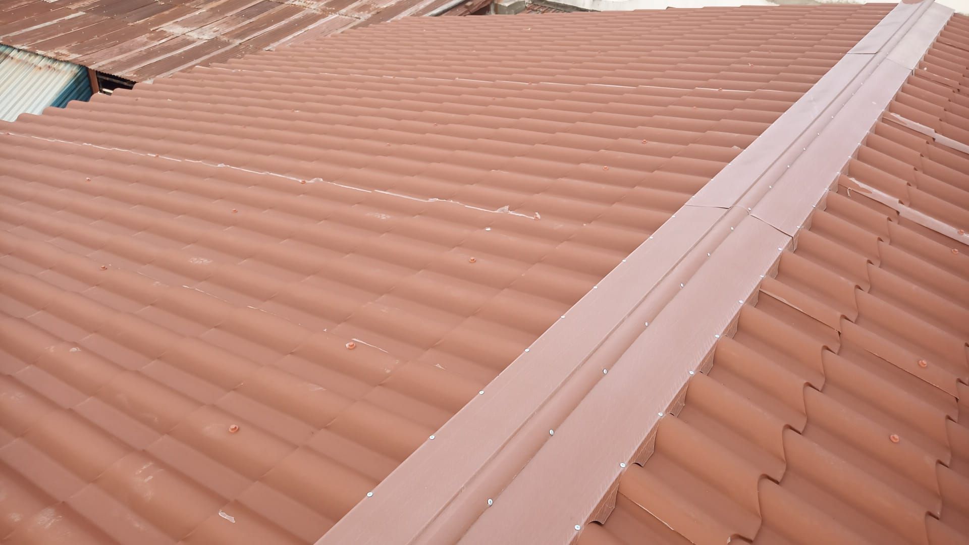 Telhado ondulado marrom com uma faixa metálica central de vedação.