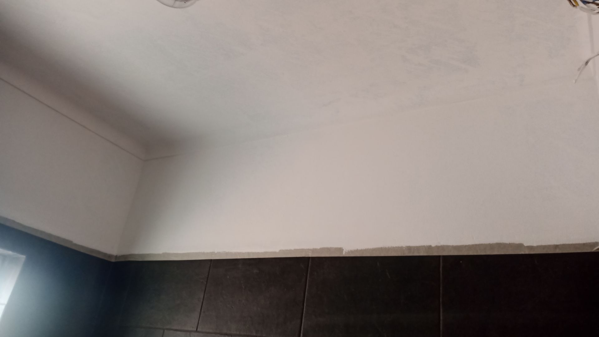 Teto e parede brancos encontram azulejos escuros, vista de canto.