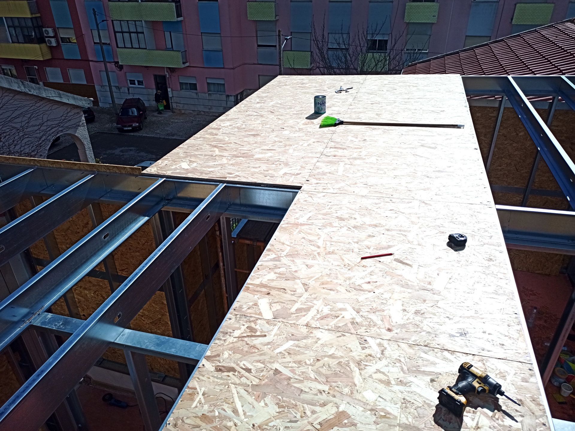 Vista aérea de um telhado em construção. Painéis de madeira estão sendo instalados em uma estrutura metálica.