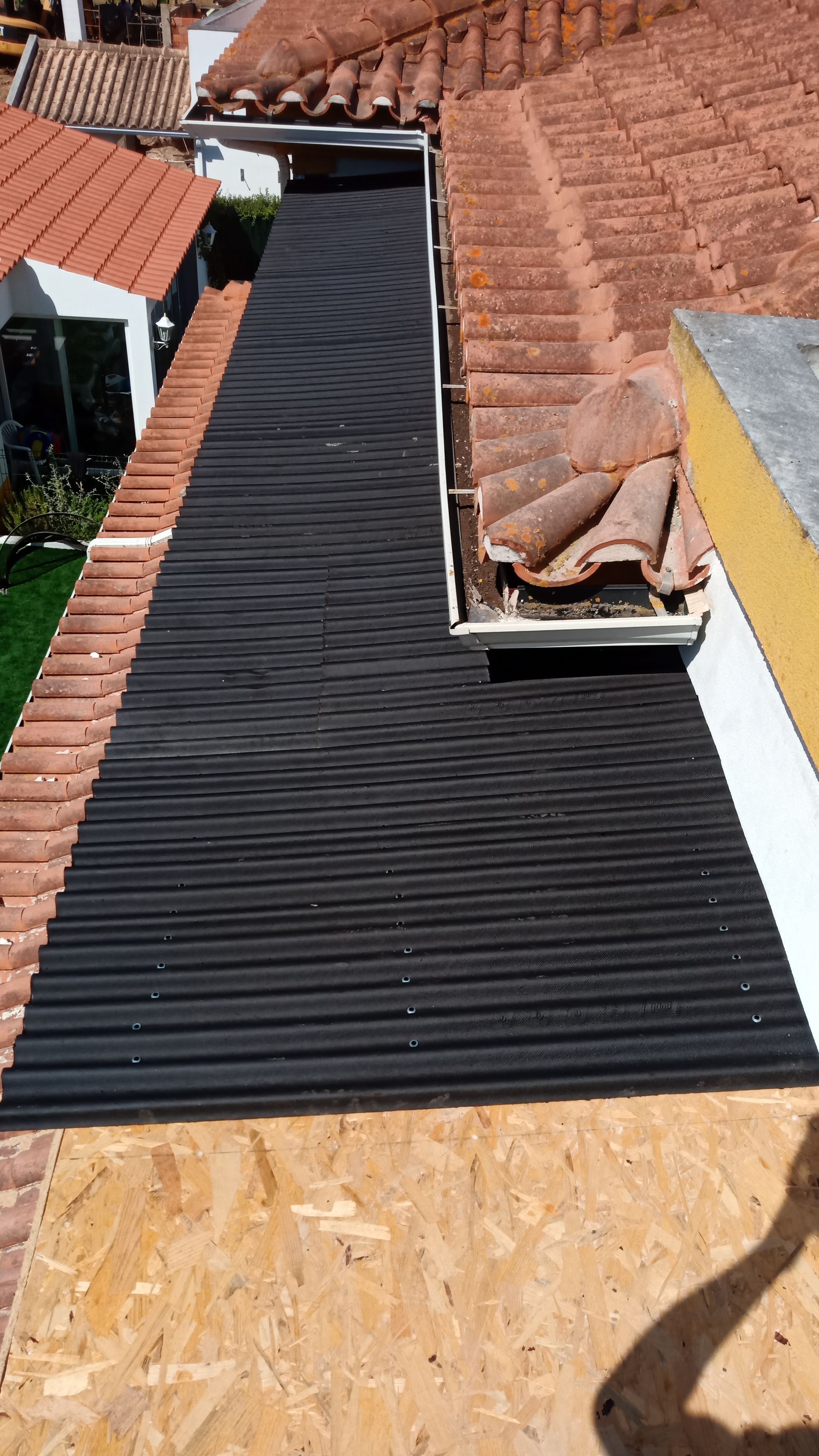 Um telhado com telhas vermelhas e uma longa seção de material ondulado preto ao lado de uma calha.