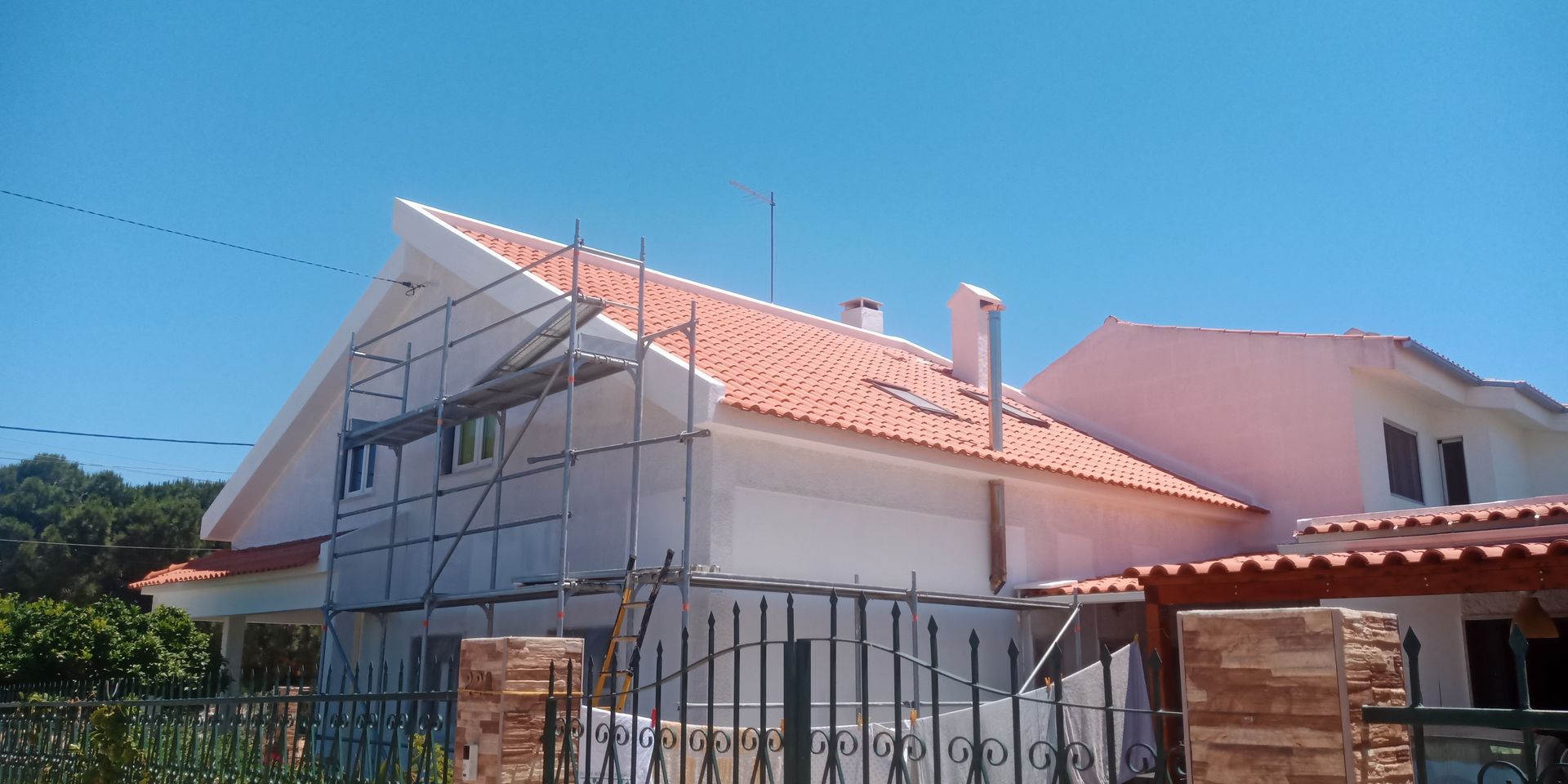 Casa com telhado de telha vermelha, andaimes e céu azul.
