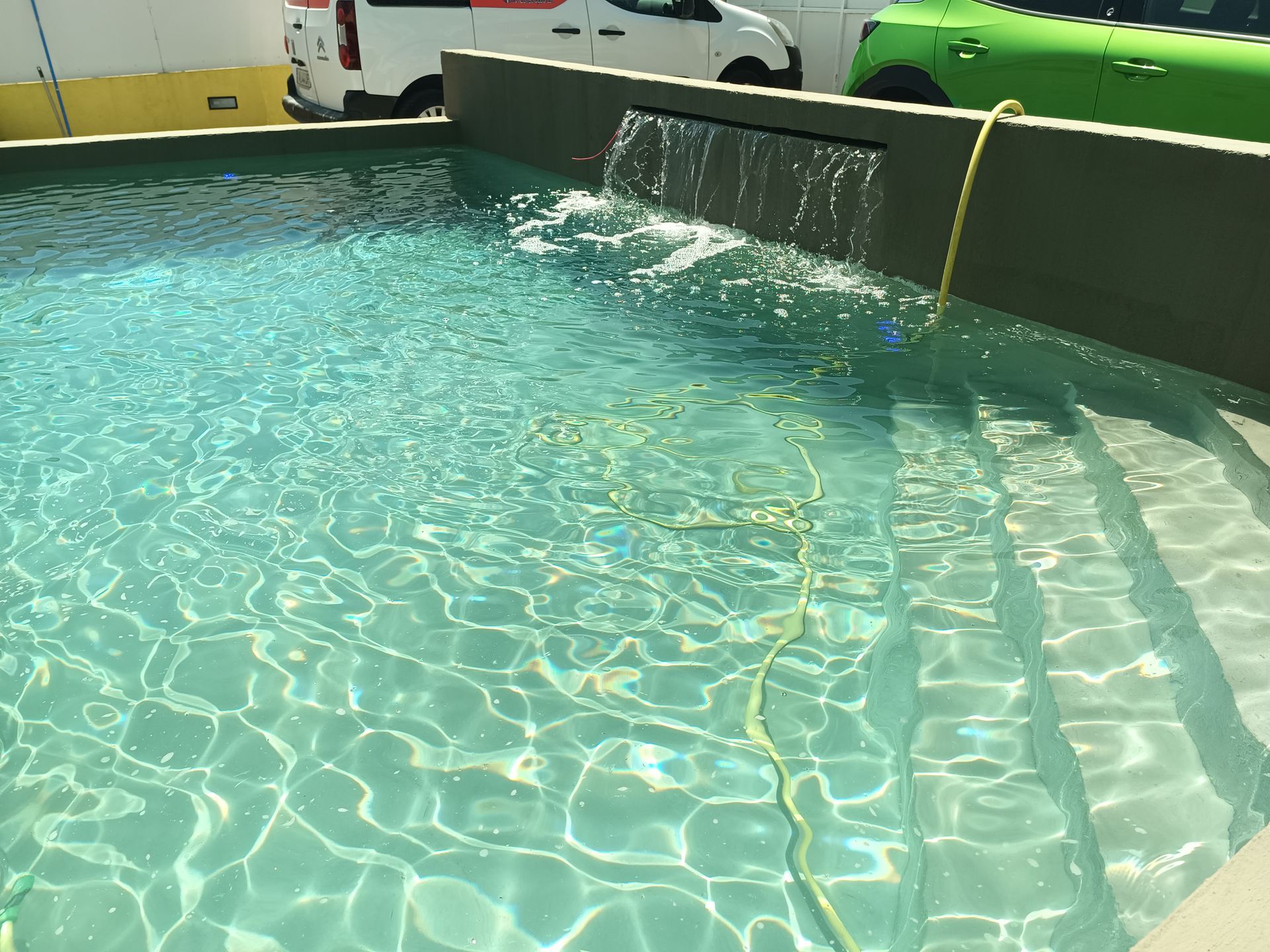 Piscina externa com água cristalina, degraus e cascata.