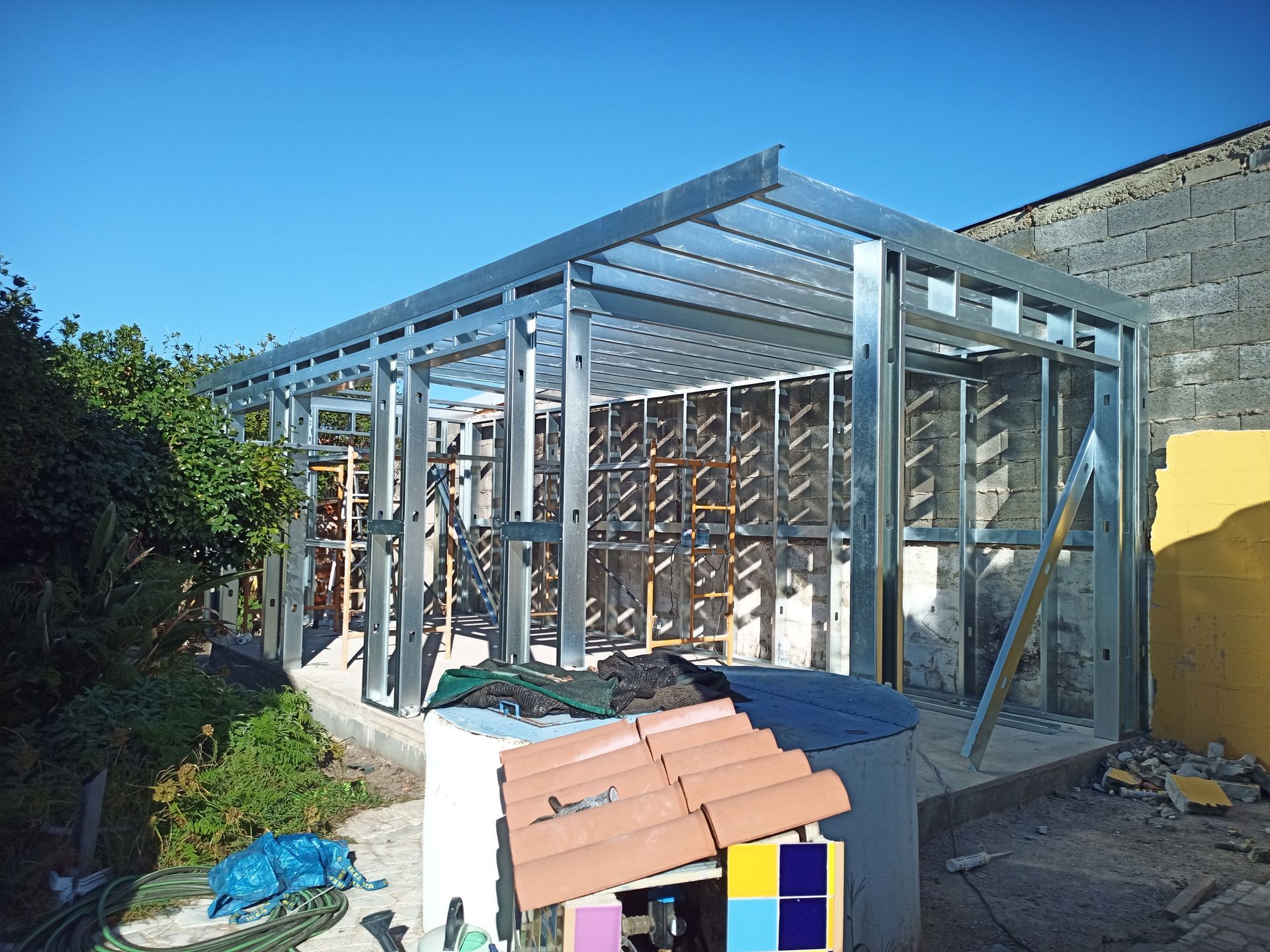 Estrutura metálica para um edifício com paredes e telhado parciais, contra uma parede amarela.