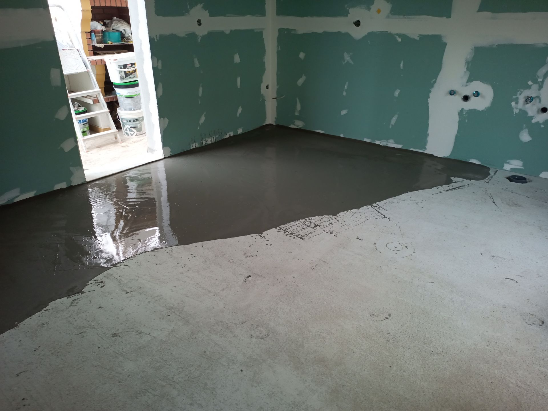 Piso de concreto cinza recém-despejado em um cômodo com paredes inacabadas e uma porta aberta.