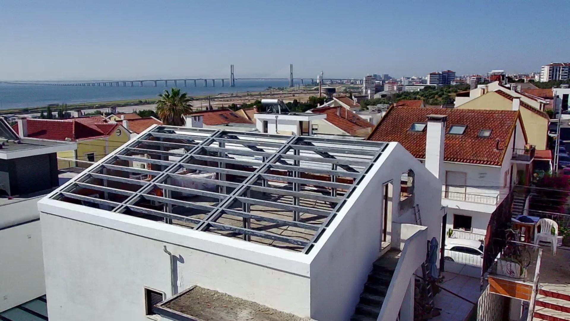 Prédio com cobertura de estrutura metálica aparente em uma cidade com vista para uma ponte e para o mar.