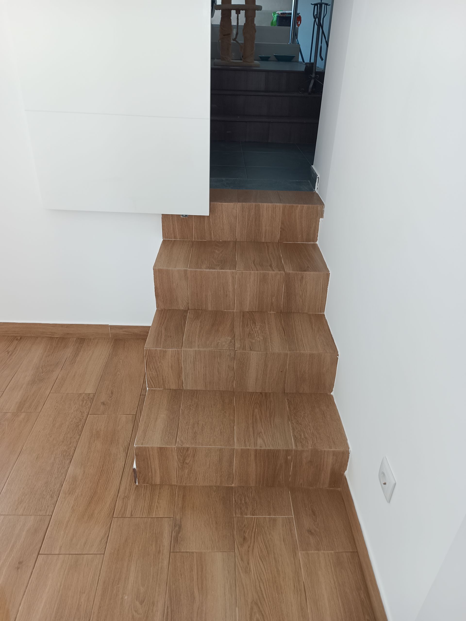 Escada revestida com azulejos marrons que leva a um andar superior a partir de um cômodo com piso de azulejos da mesma cor. Paredes brancas.