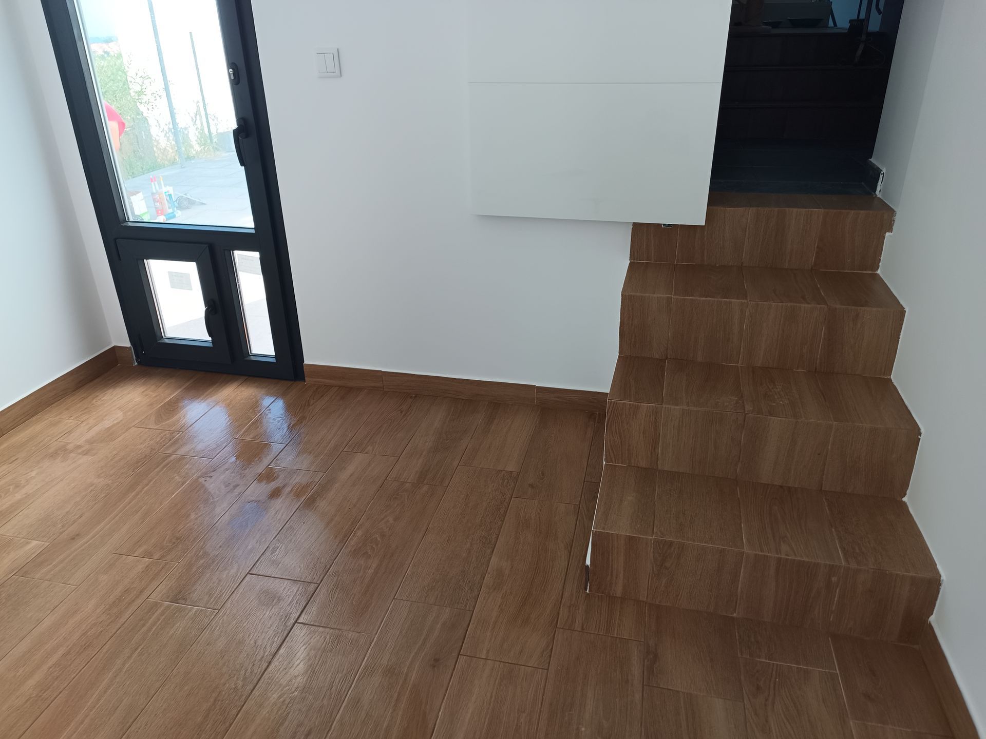 Quarto interior com piso de madeira, escadas, porta e paredes brancas.