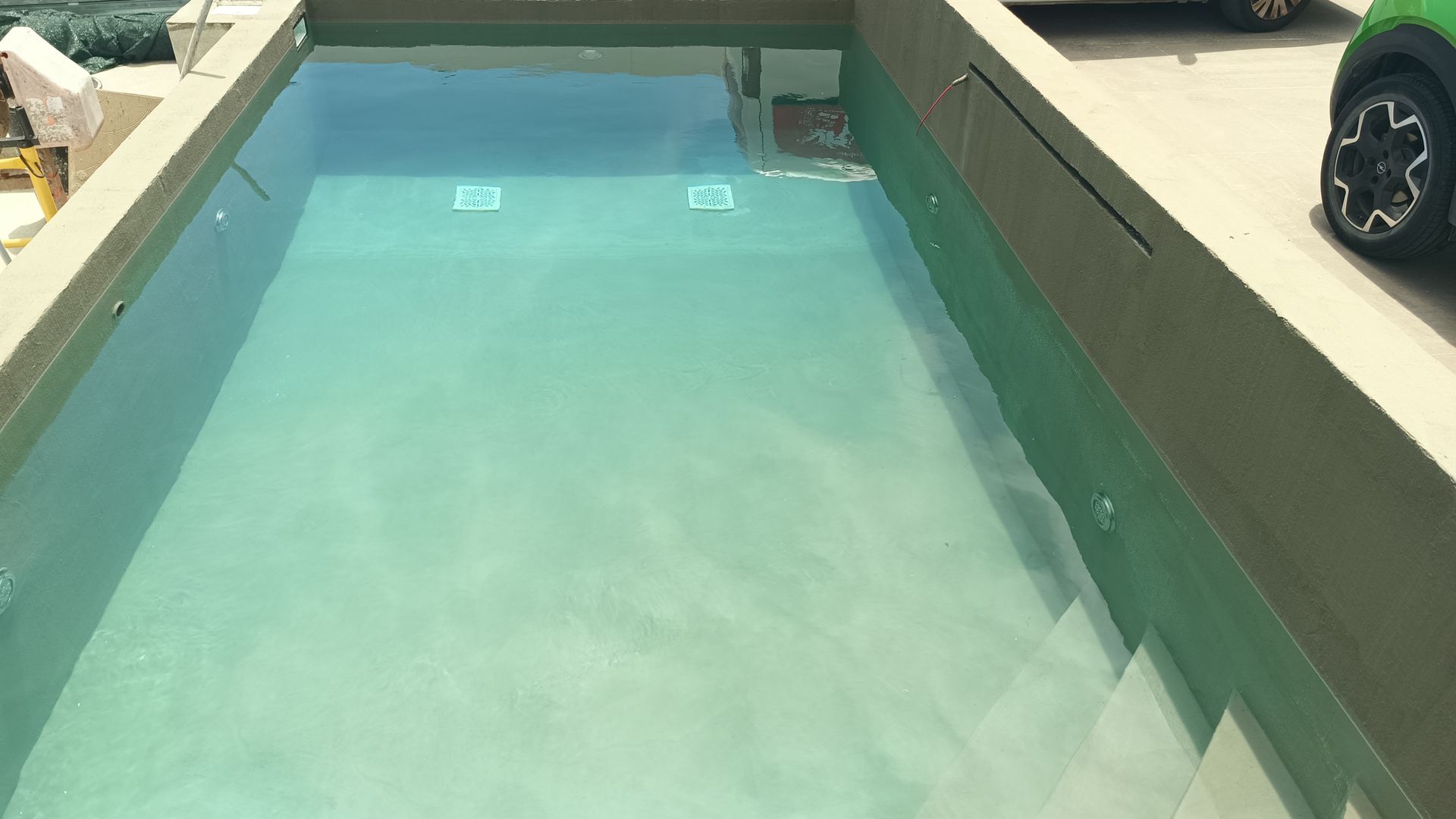 Uma piscina retangular com água turquesa, construída em um pátio de concreto.