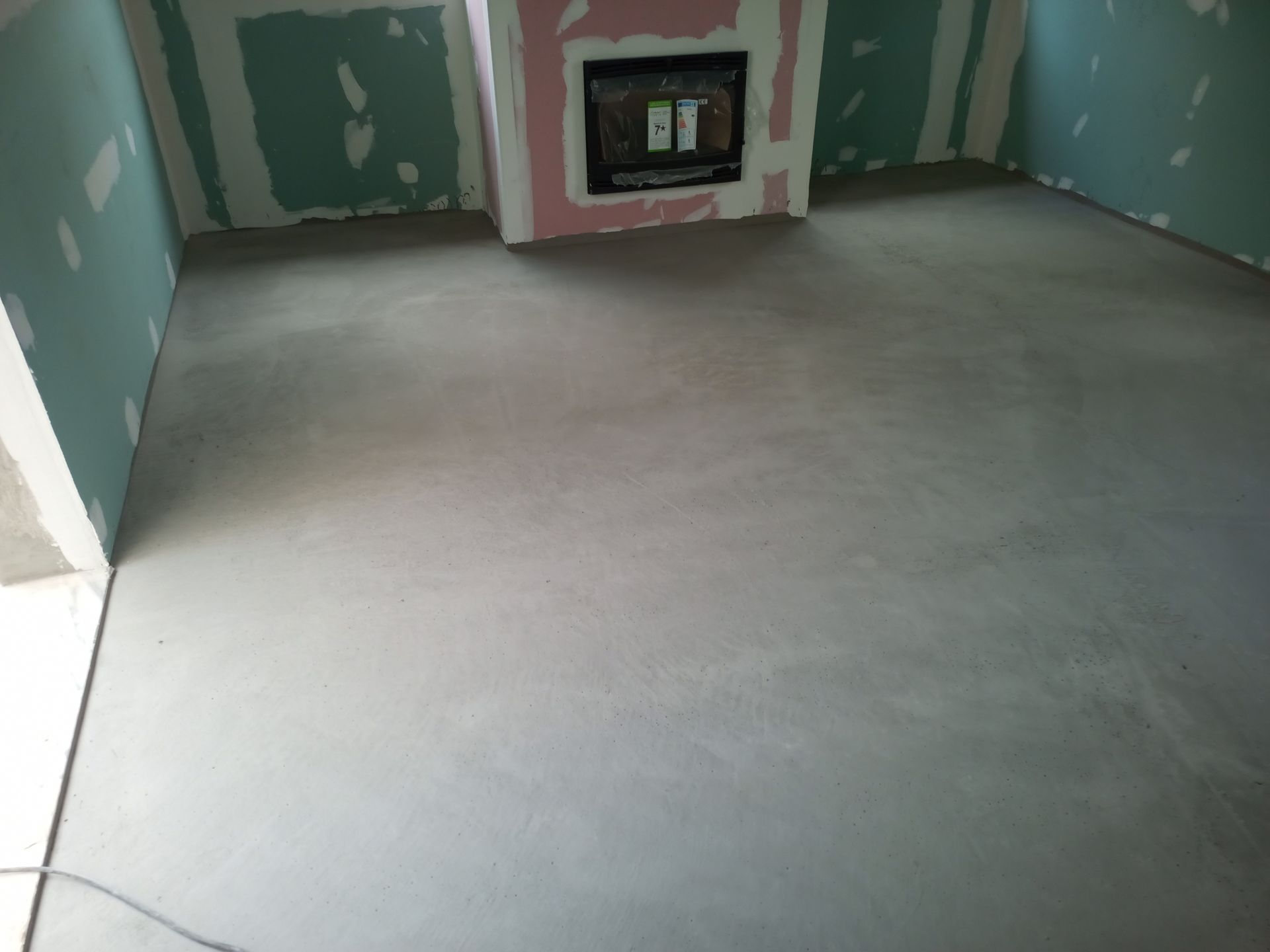 Uma sala com piso de concreto cinza, lareira e paredes de gesso com fita verde.
