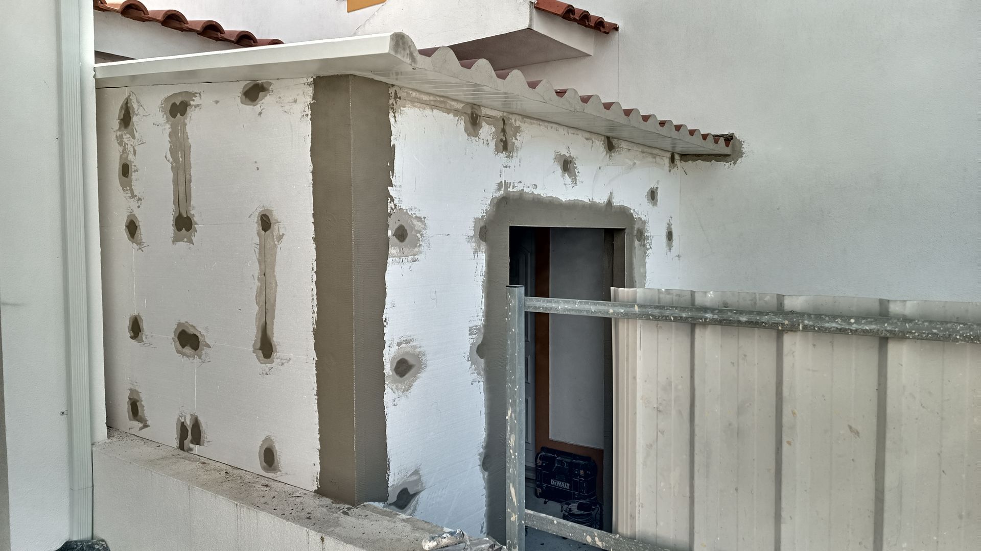 Parede externa em construção com isolamento aparente, porta e um pequeno telhado.