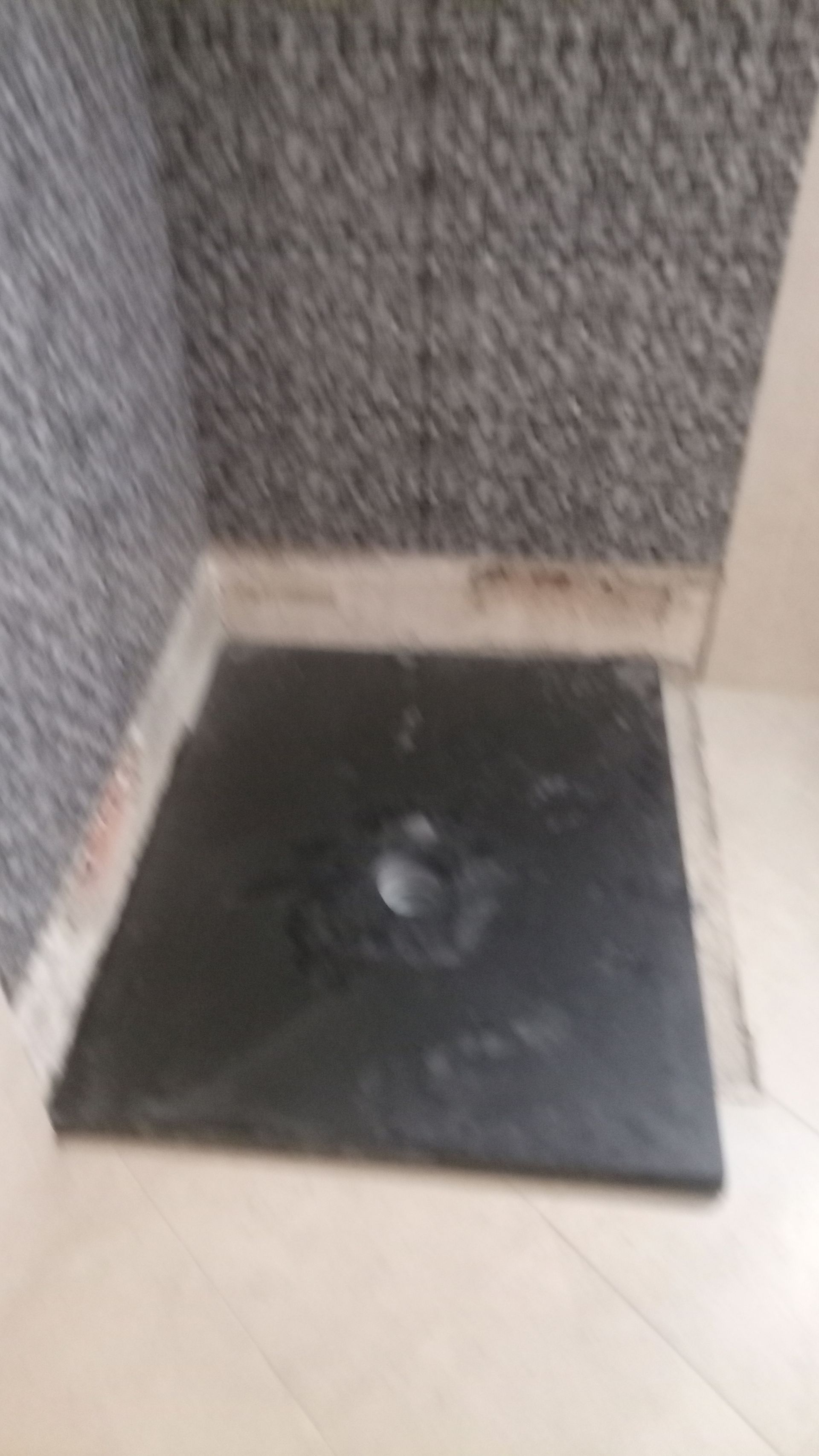 Base de chuveiro preta em um canto com parede revestida de azulejos cinza e piso branco.