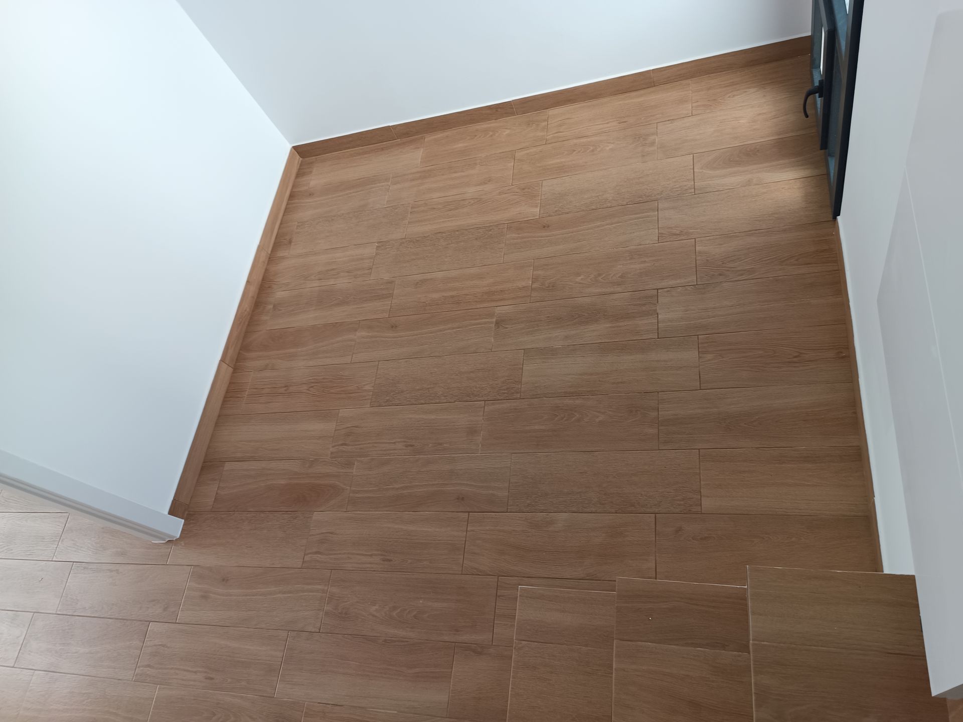 Escada de madeira vista de cima, paredes bege e corrimão de metal à direita.