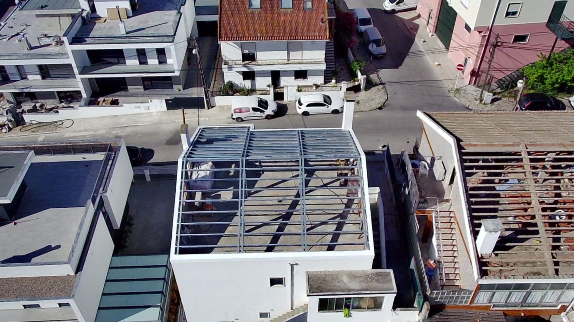 Vista aérea de um edifício branco em construção, com a estrutura metálica visível. Os edifícios e ruas circundantes também são visíveis.