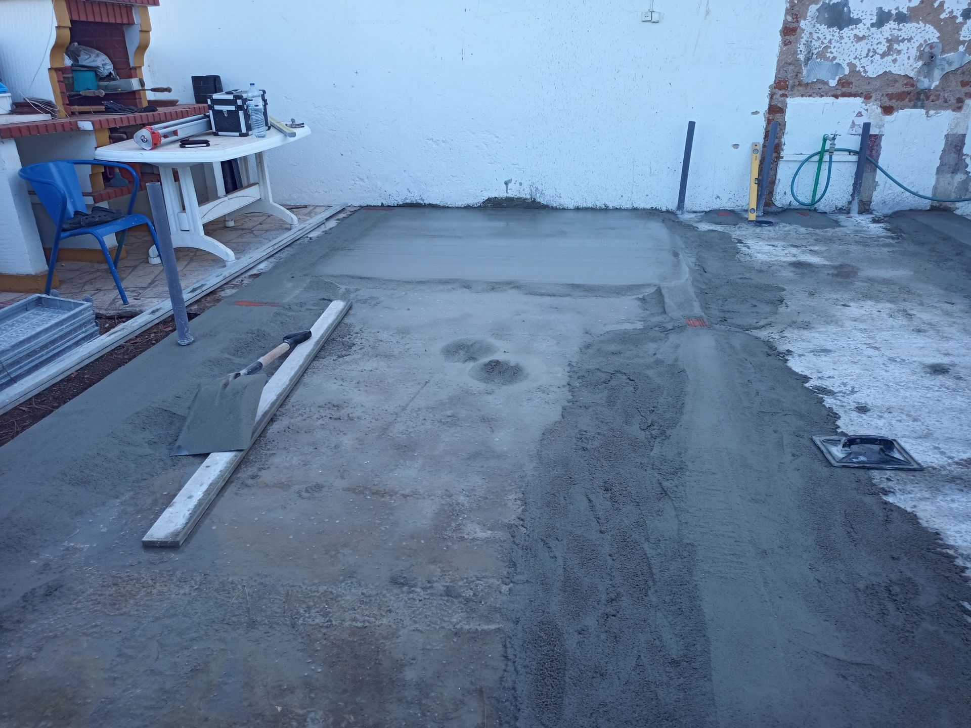 Pátio de concreto em construção; cimento cinza sendo nivelado com uma espátula e régua.