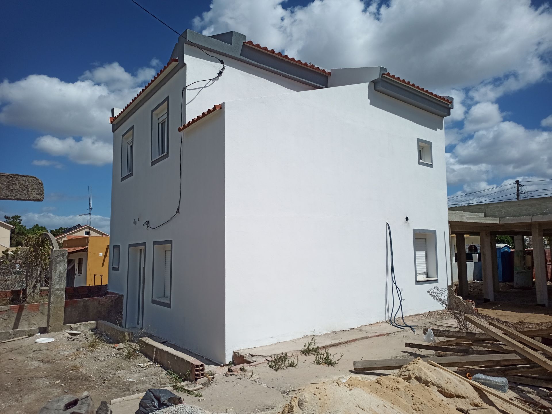 Casa branca de dois andares em construção contra um céu parcialmente nublado. Telhado e janelas de telha vermelha são visíveis.
