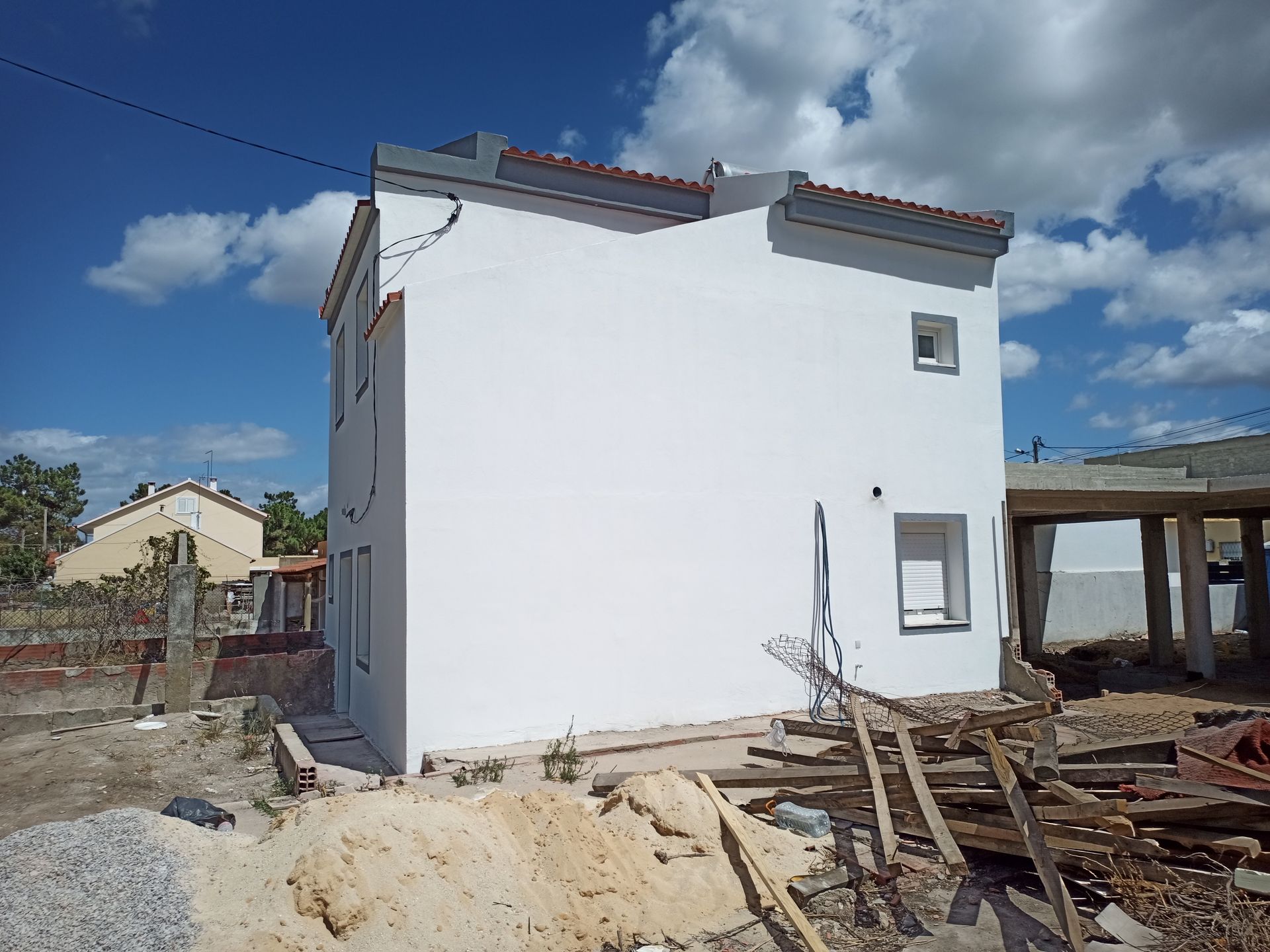 Prédio branco de dois andares em construção, com céu azul ao fundo. Tábuas de madeira e entulho em primeiro plano.