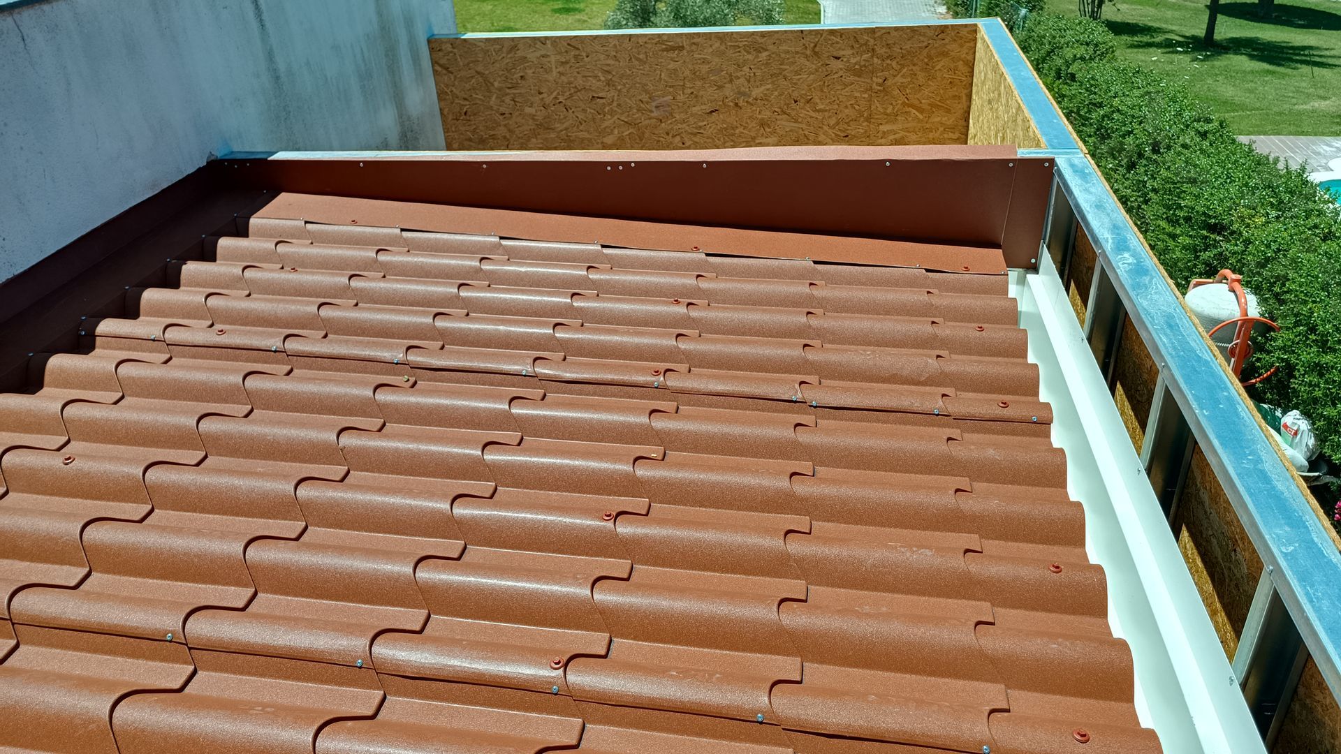 Telhado de telhas marrons com detalhes em metal e vista para a vegetação.