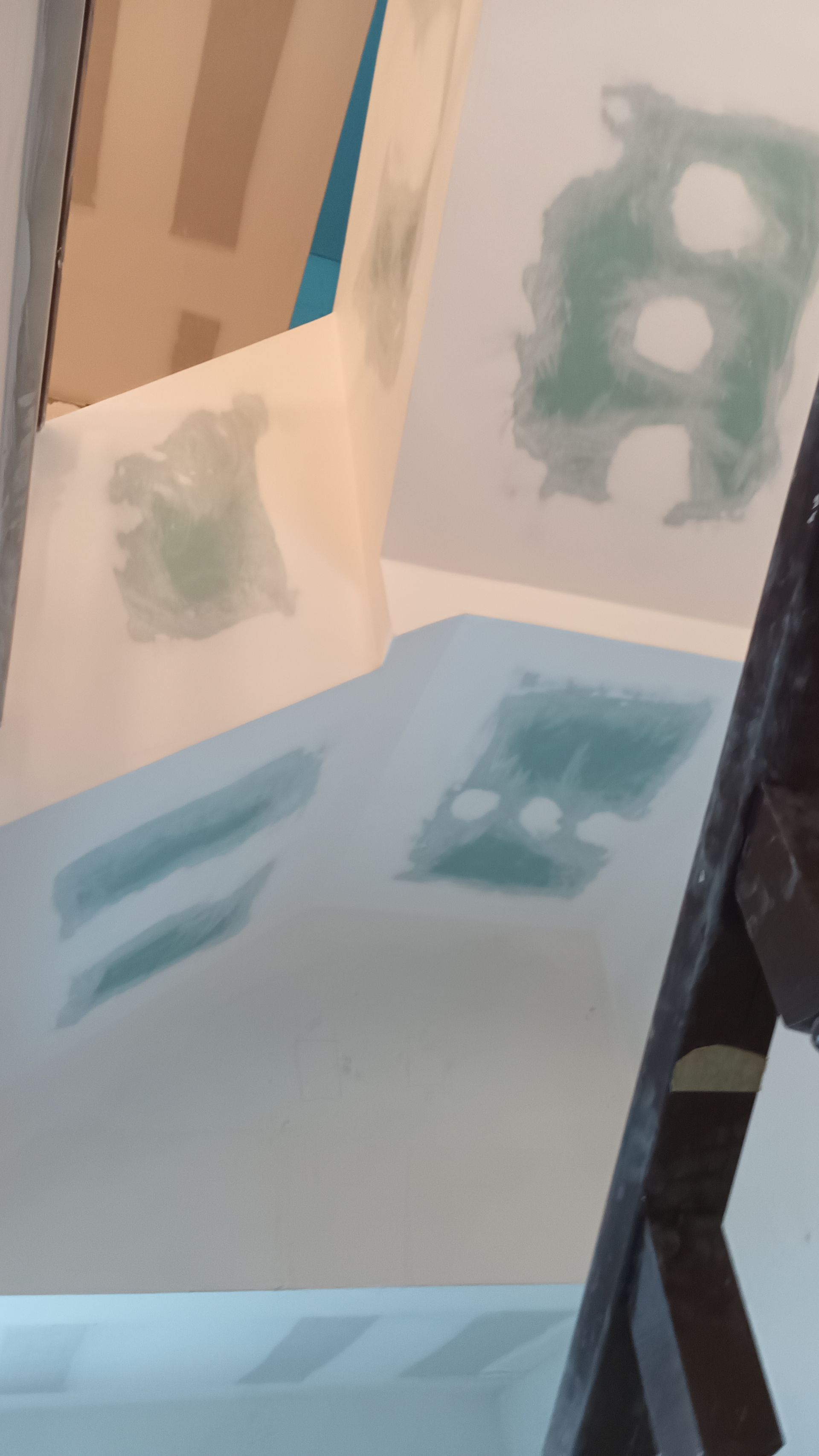 Paredes internas com drywall remendado, em vários tons de branco e verde. Uma escada de madeira está à direita.