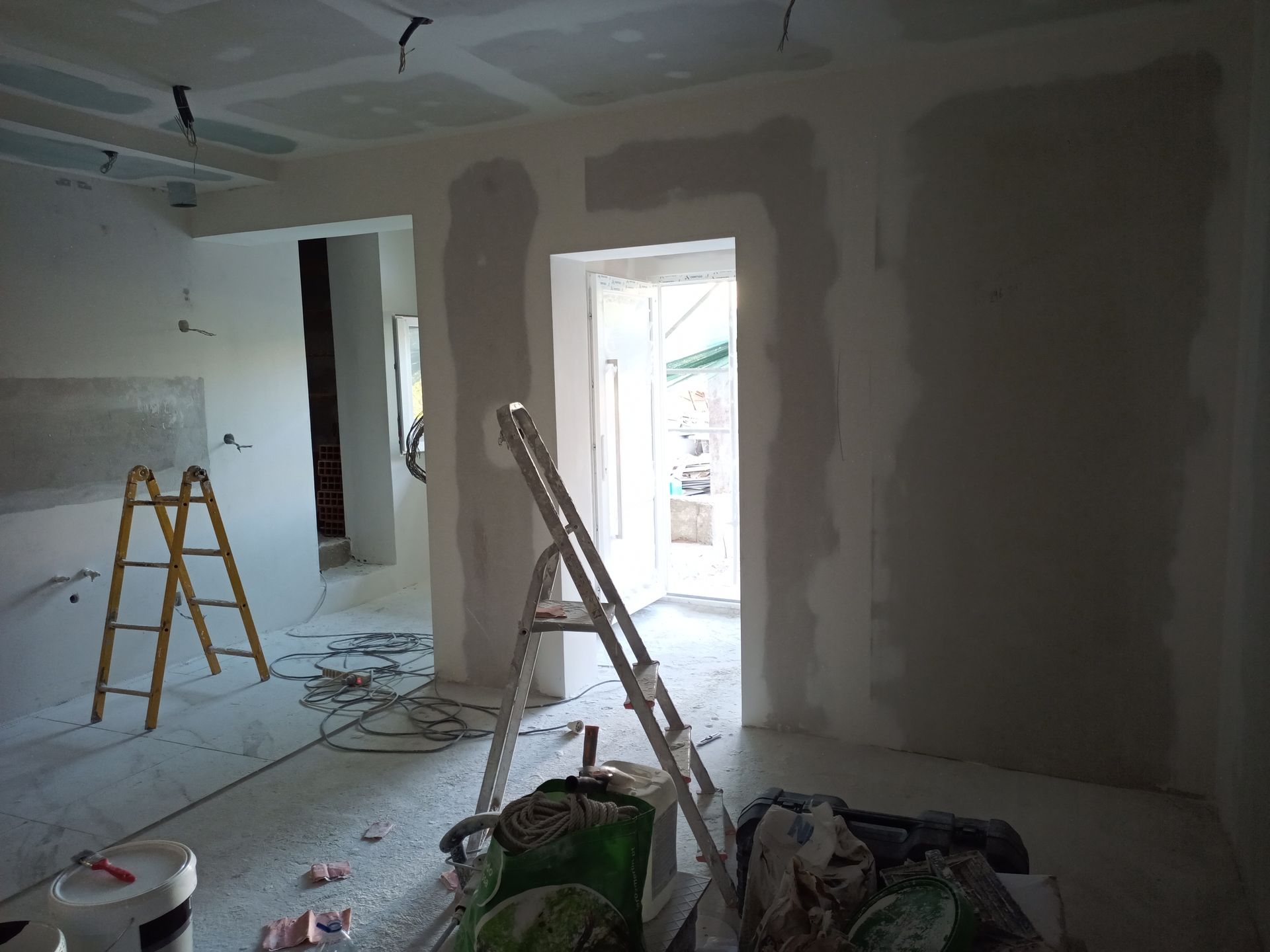 Reforma interna em andamento, com instalação de drywall nas paredes e no teto. Escadas, ferramentas e entulho visíveis.