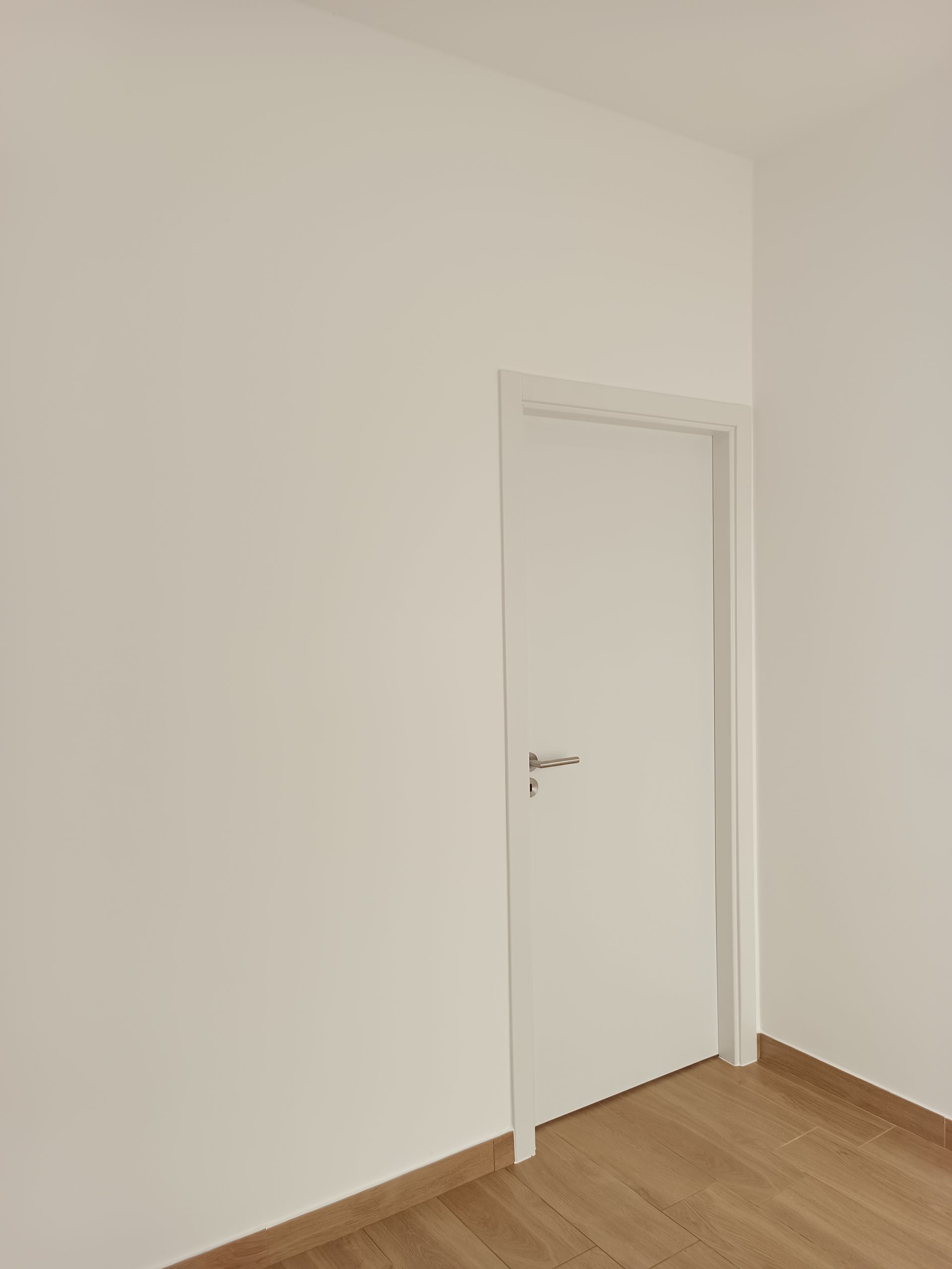 Porta branca em um quarto com paredes brancas e piso de madeira.