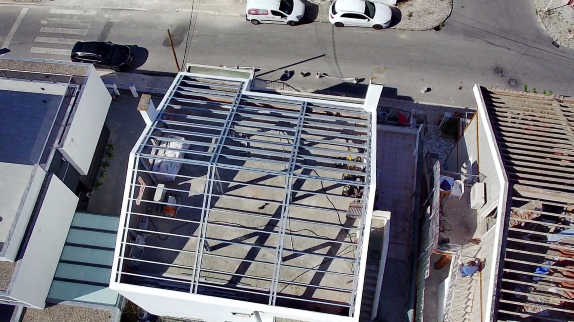 Vista aérea de um edifício em construção, com cobertura de estrutura metálica e rua com carros estacionados.