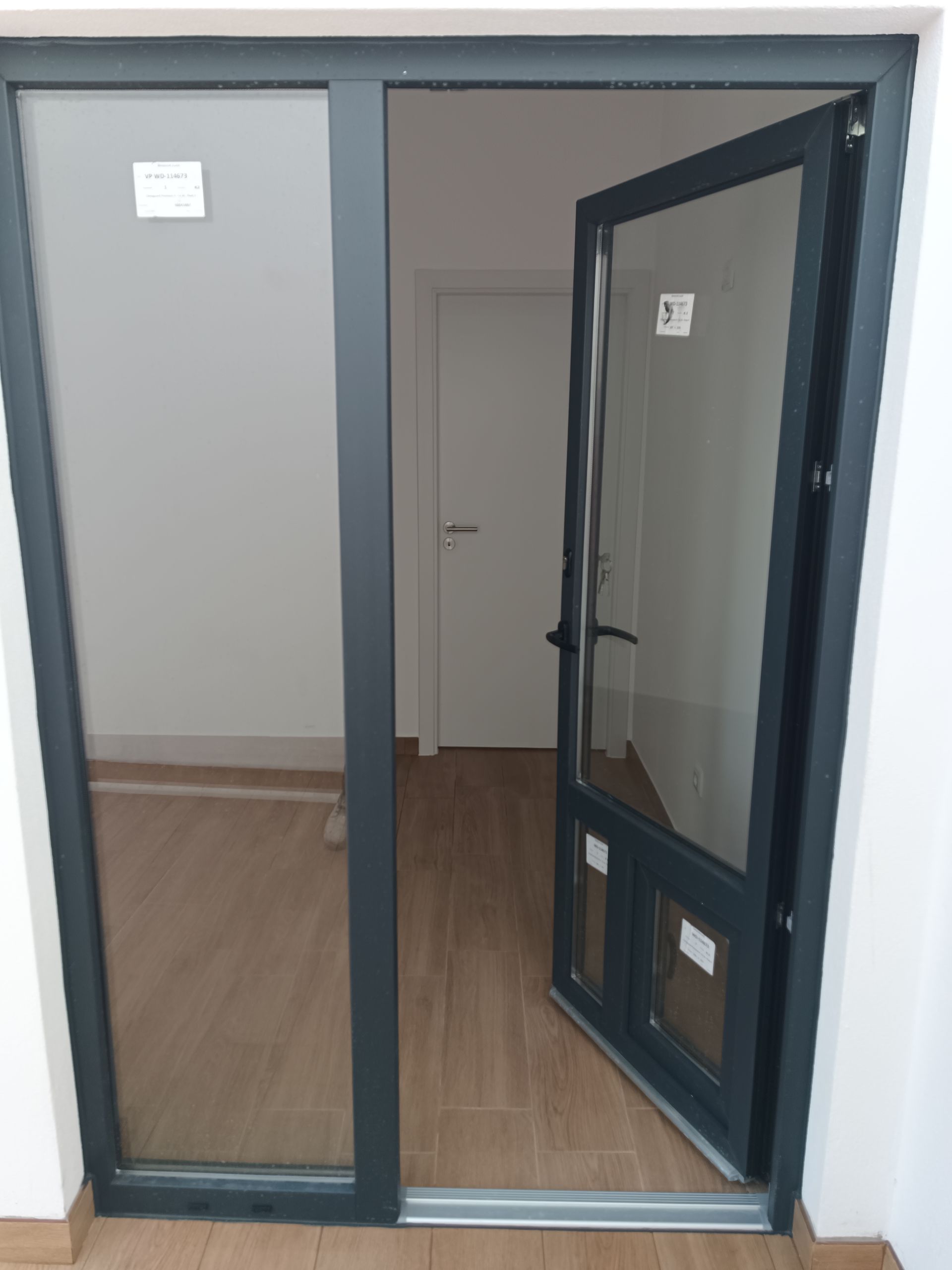 Porta de vidro com uma das folhas abertas, revelando um interior com paredes claras e piso que imita madeira.