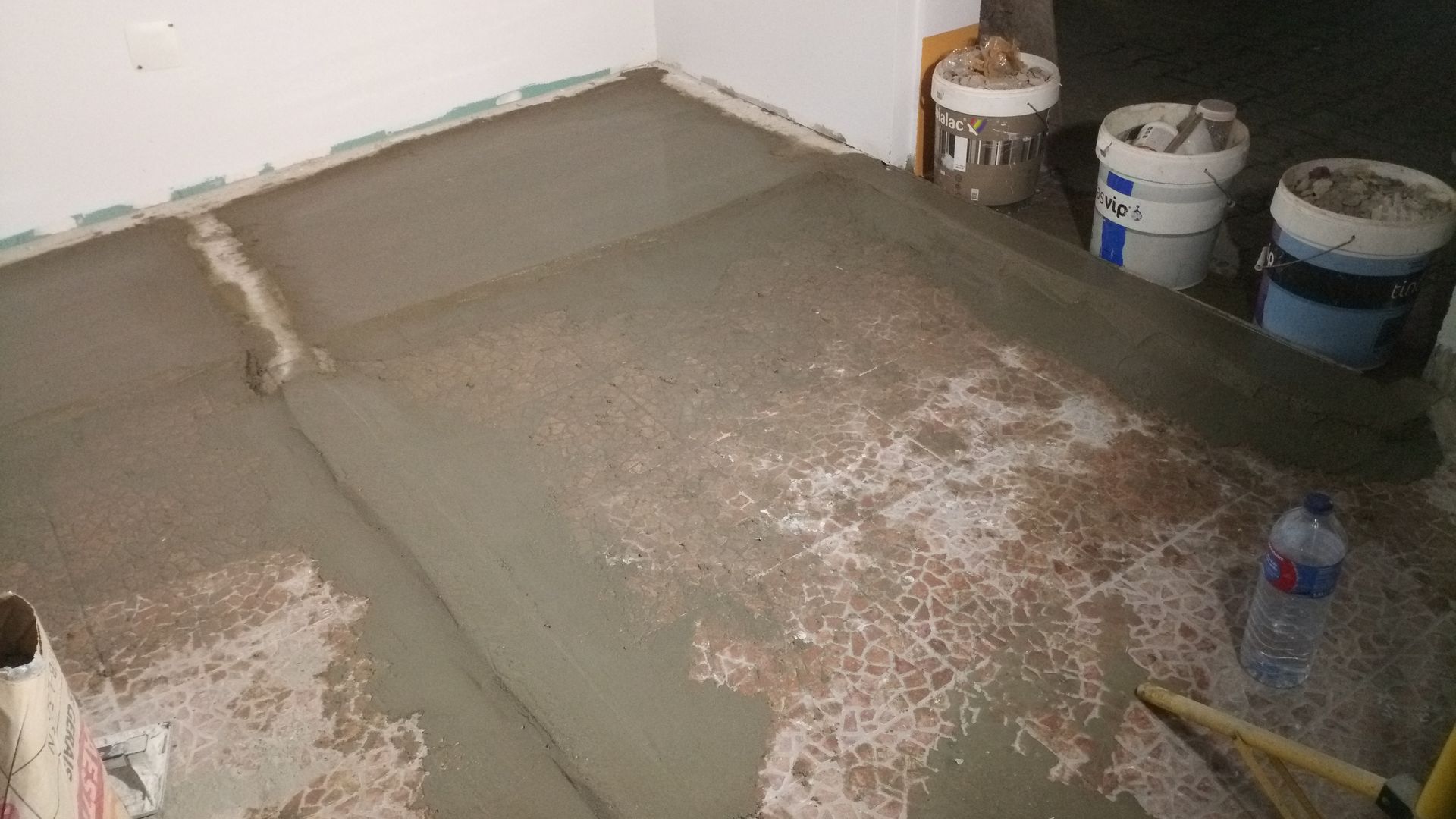 Piso de concreto recém-lançado; baldes e ferramentas por perto, interior de um canteiro de obras.