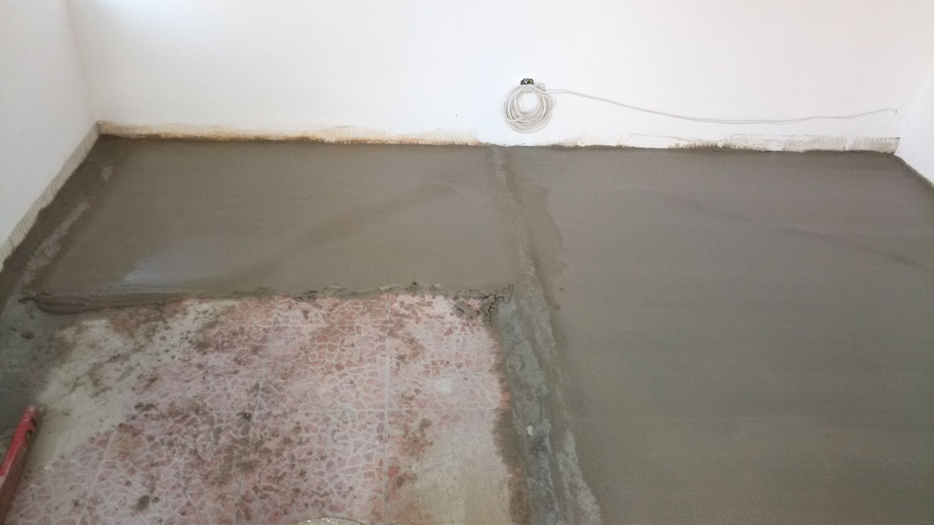 Piso de concreto recém-moldado em um cômodo, encontrando uma seção mais antiga e rústica; paredes brancas.