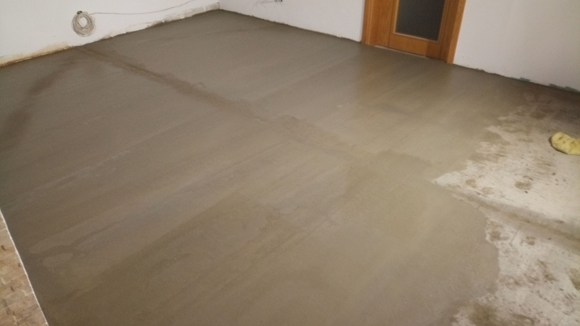 Piso de concreto recém-moldado em um cômodo, com uma porta visível ao fundo.