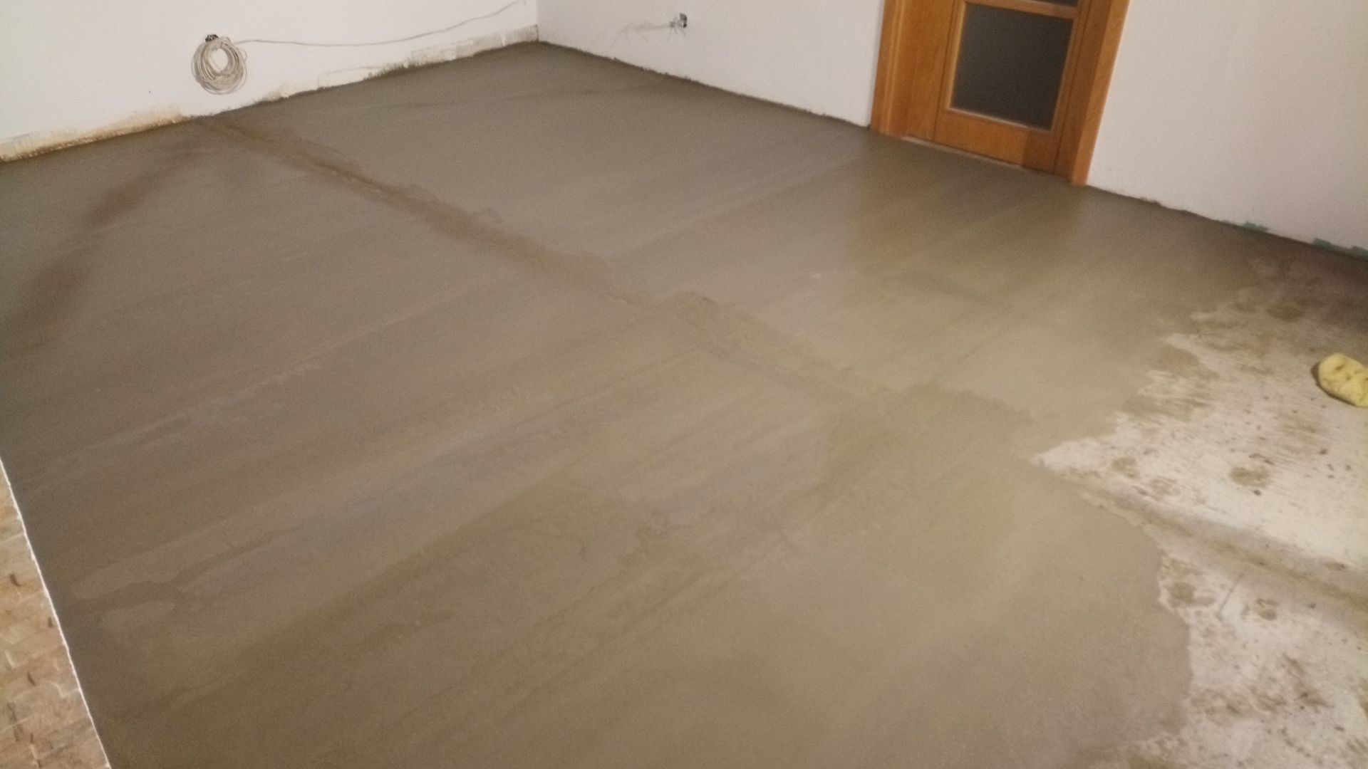 Piso de concreto recém-moldado em um cômodo, de cor cinza claro, com porta e paredes visíveis.