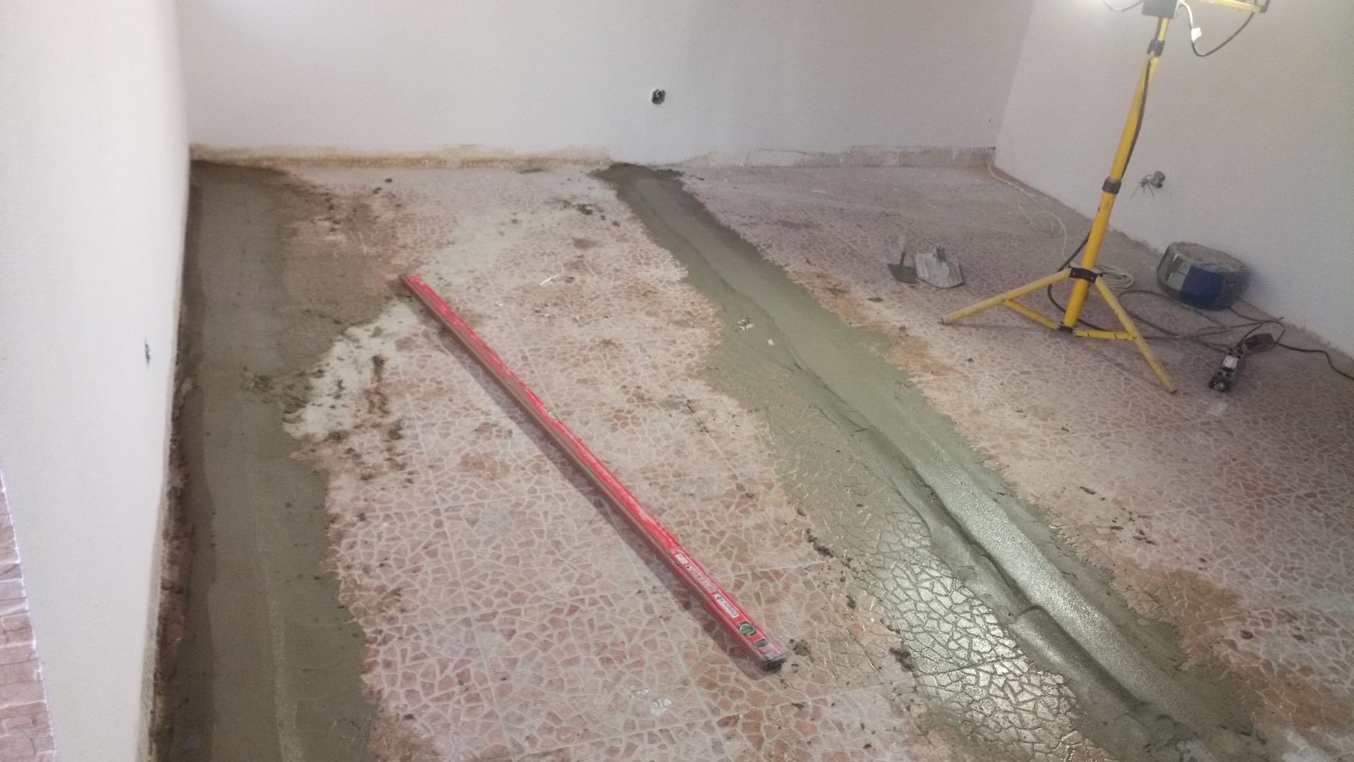 Obra de piso de concreto em andamento; cimento fresco, nível e luz de trabalho em um cômodo.